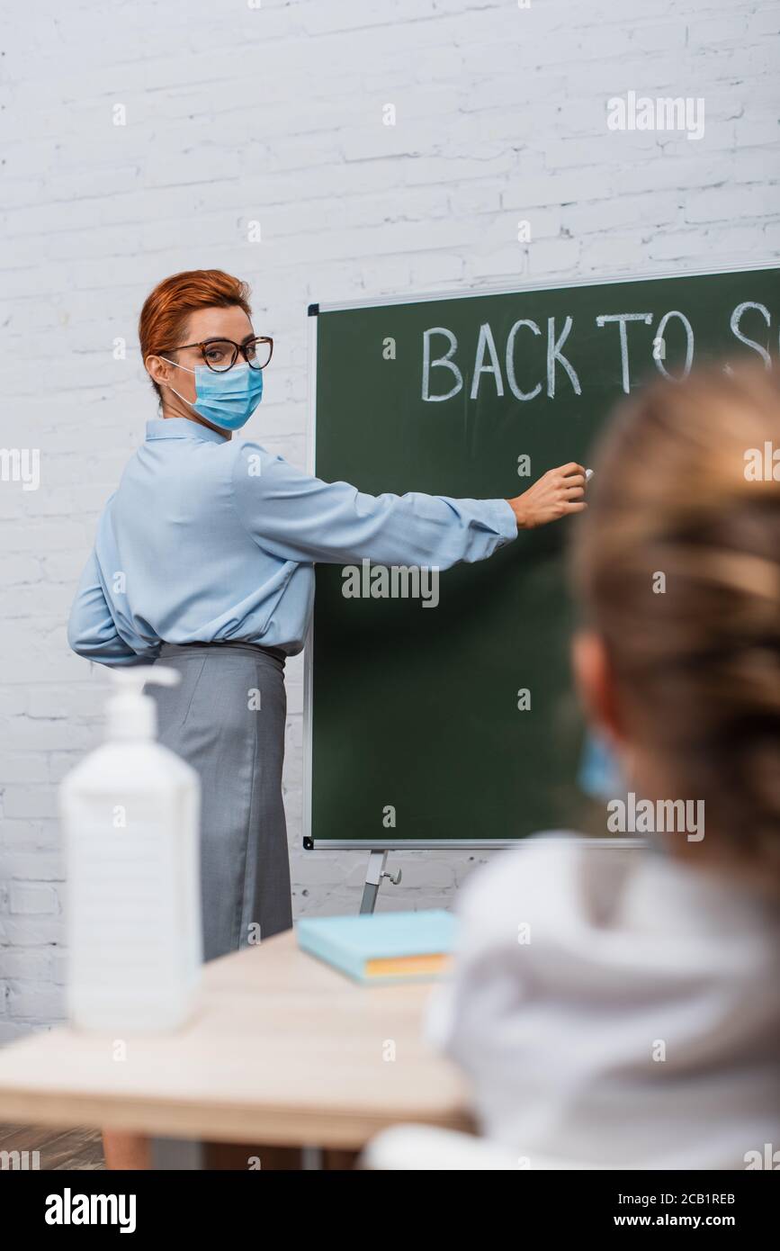 back view of schoolgirl, and teacher in medical mask writing on ...