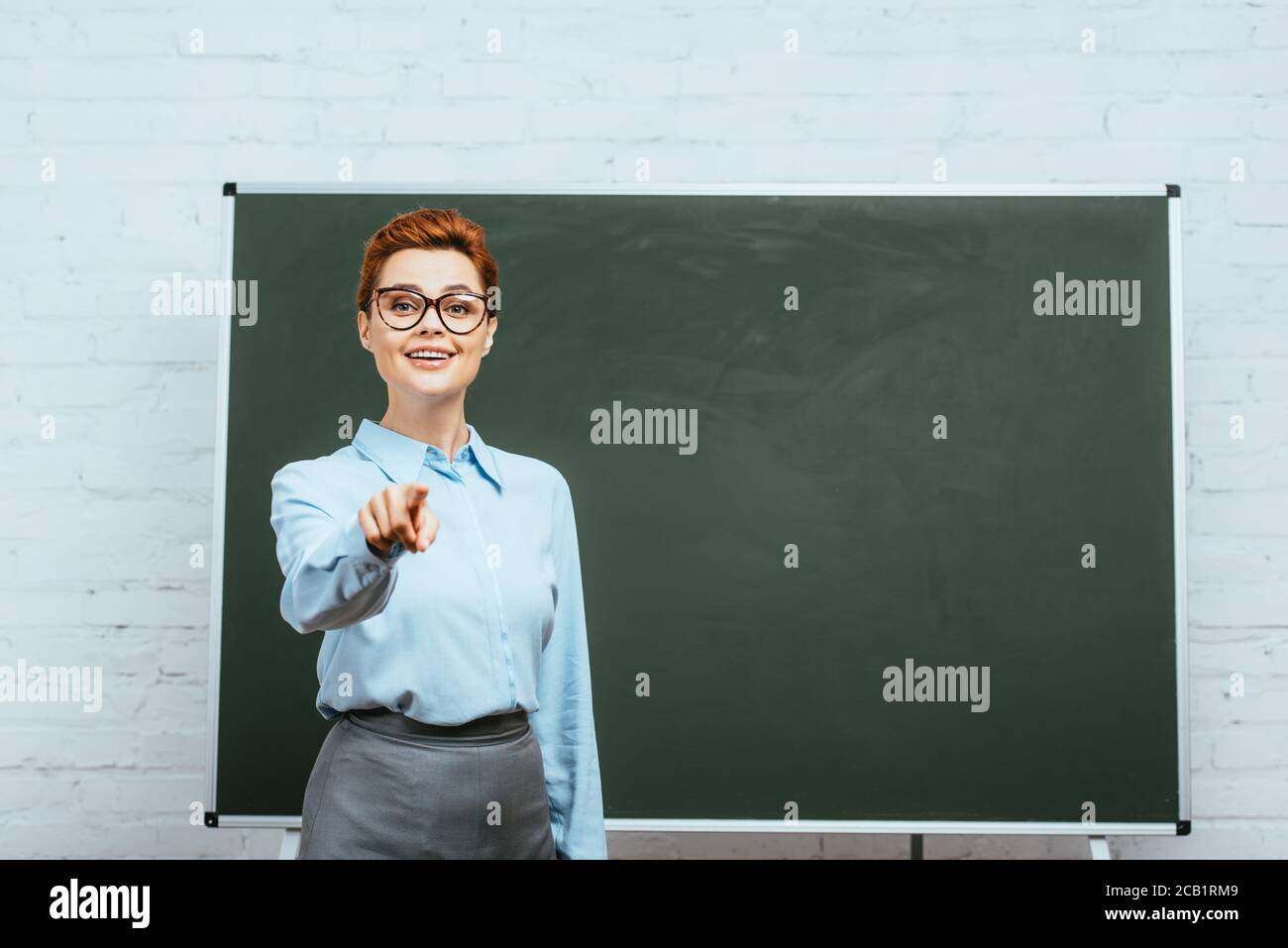 Pointing Near smiling teacher looking at camera and pointing with finger near ...