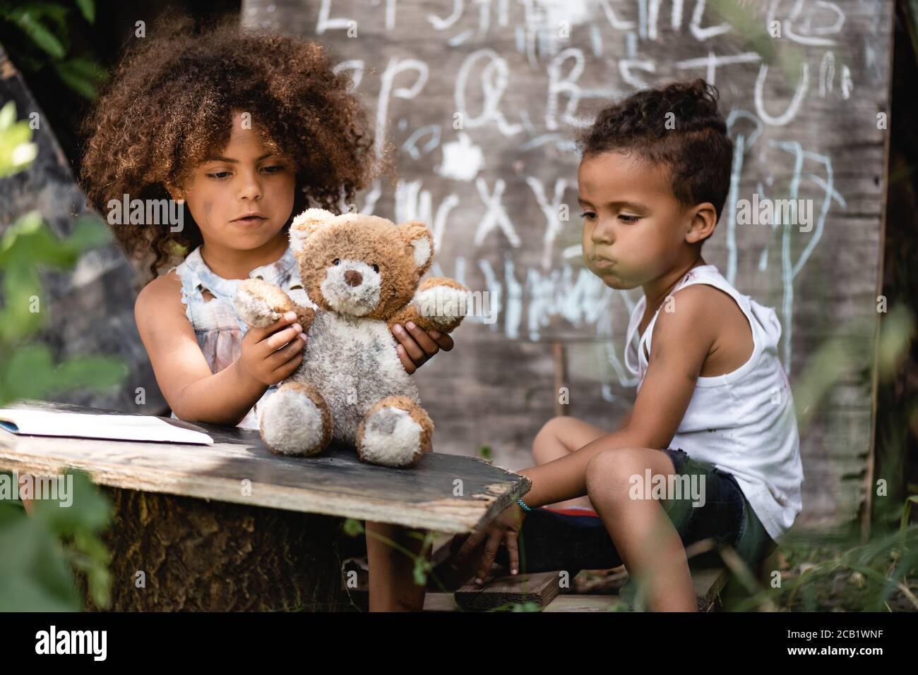 selective focus of poor african american kid playing with dirty teddy bear near brother Stock Photo
