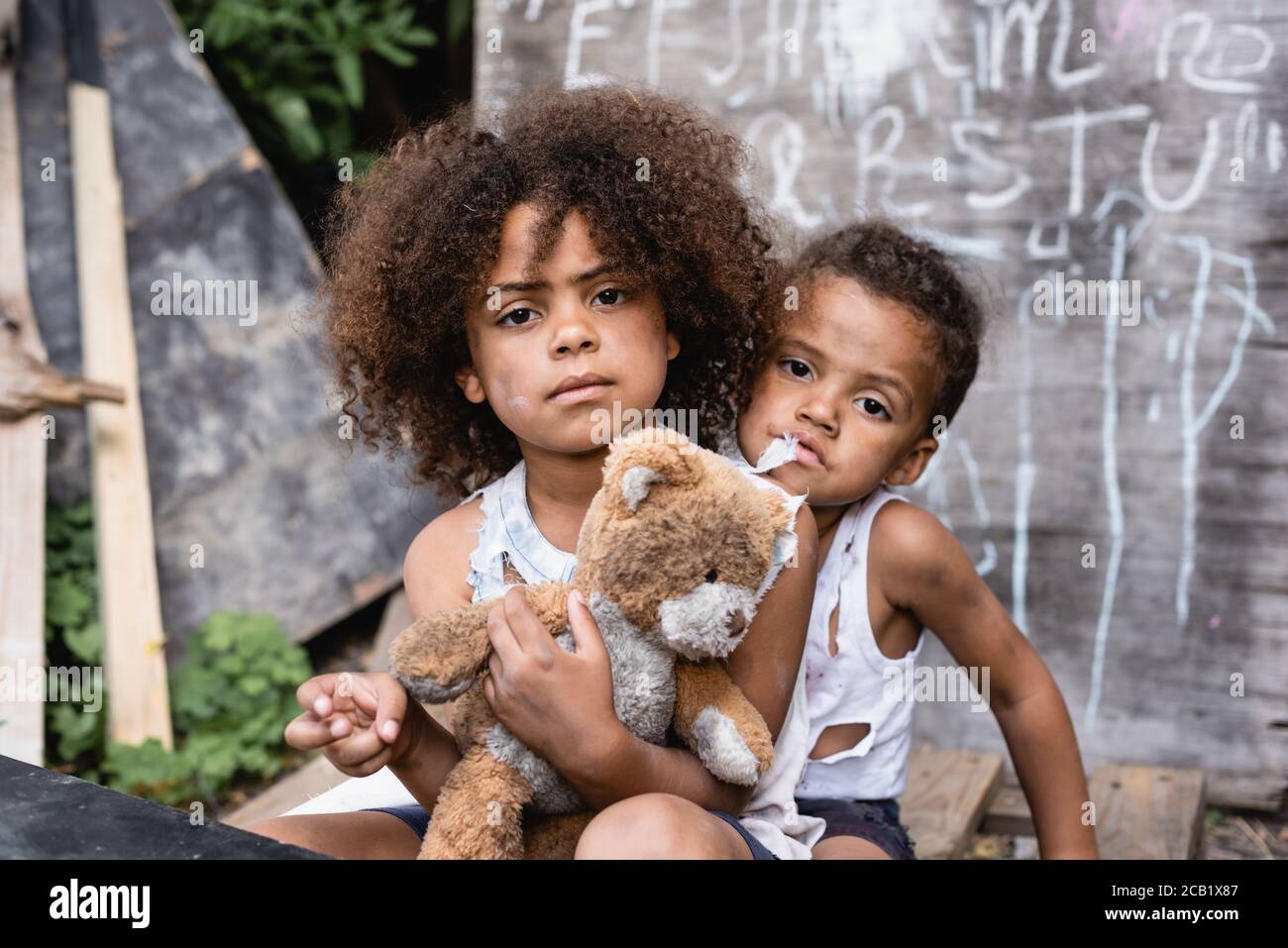 poor african american kids with dirty teddy bear looking at camera Stock Photo