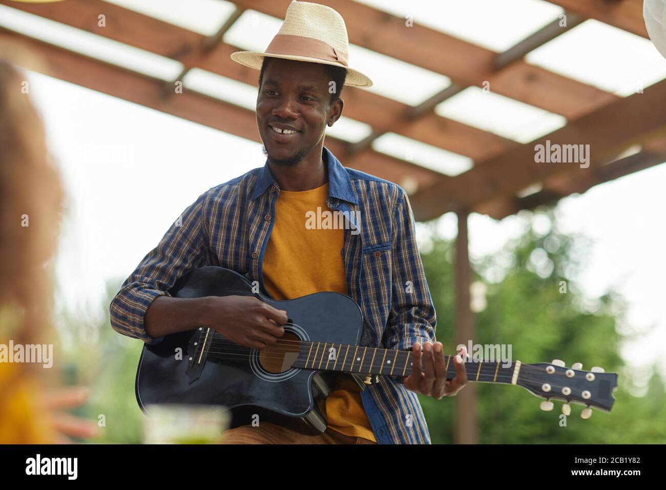 Waist up portrait of young African-American man playing guitar while enjoying dinner with friends outdoors at Summer party, copy space Stock Photo