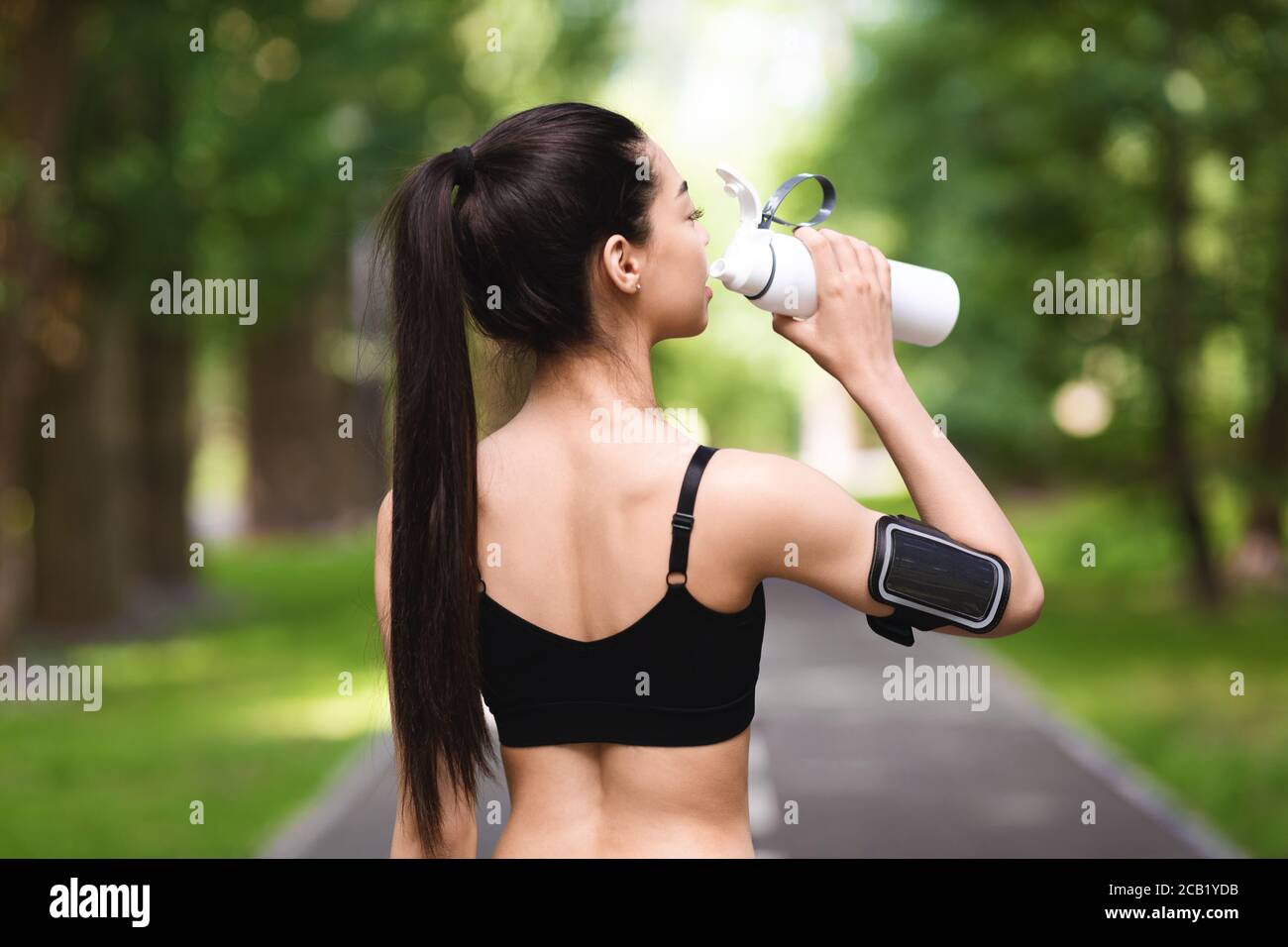 Rear view of asian fitness woman drinking water after jogging in park Stock Photo