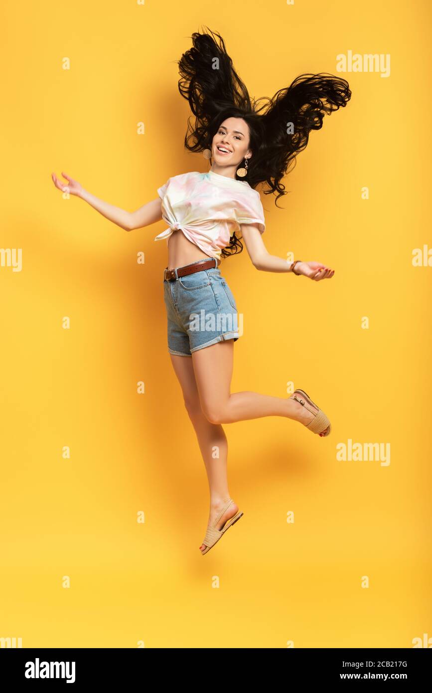full length view of happy brunette girl jumping on yellow background ...