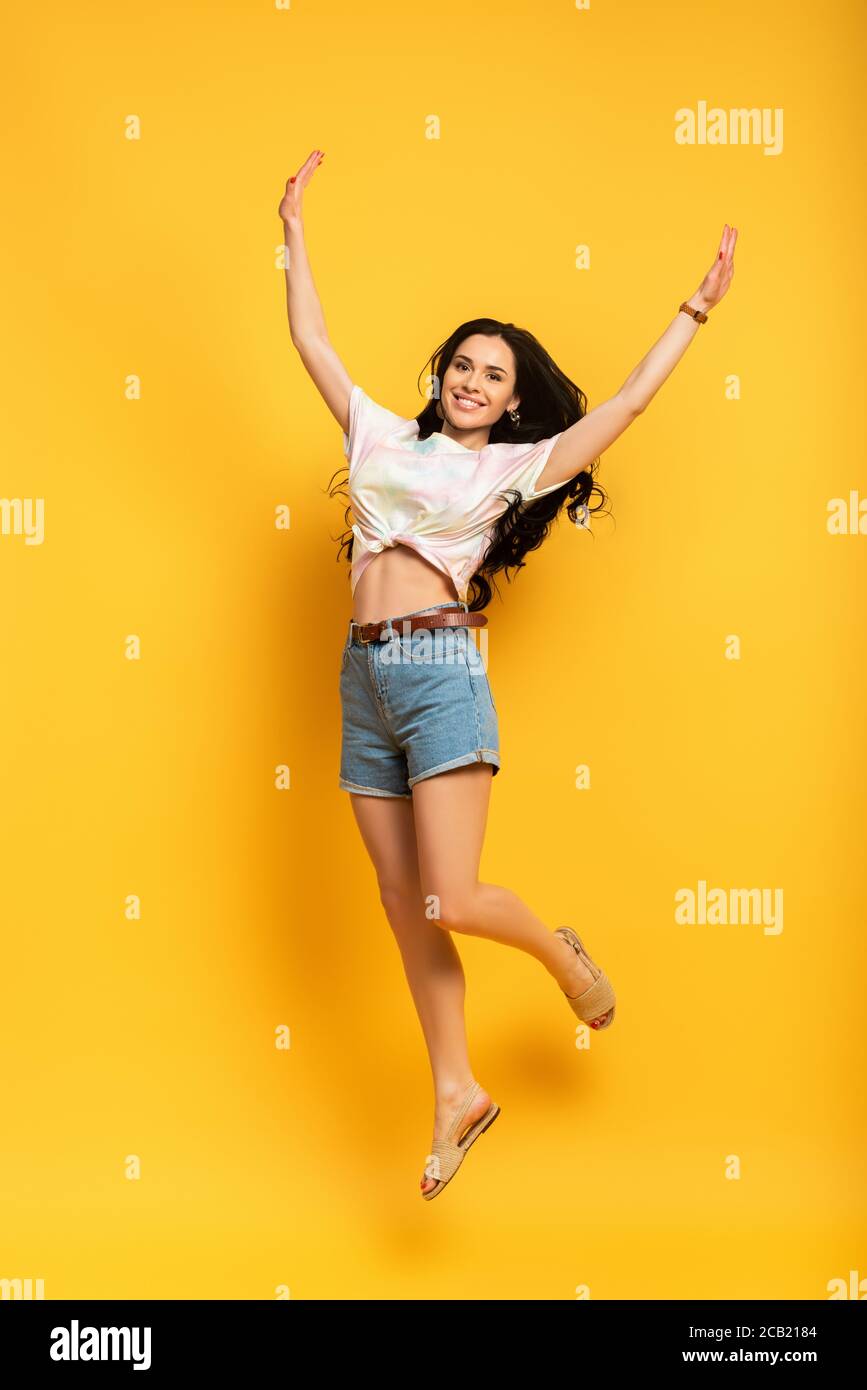 full length view of happy brunette girl jumping on yellow background ...