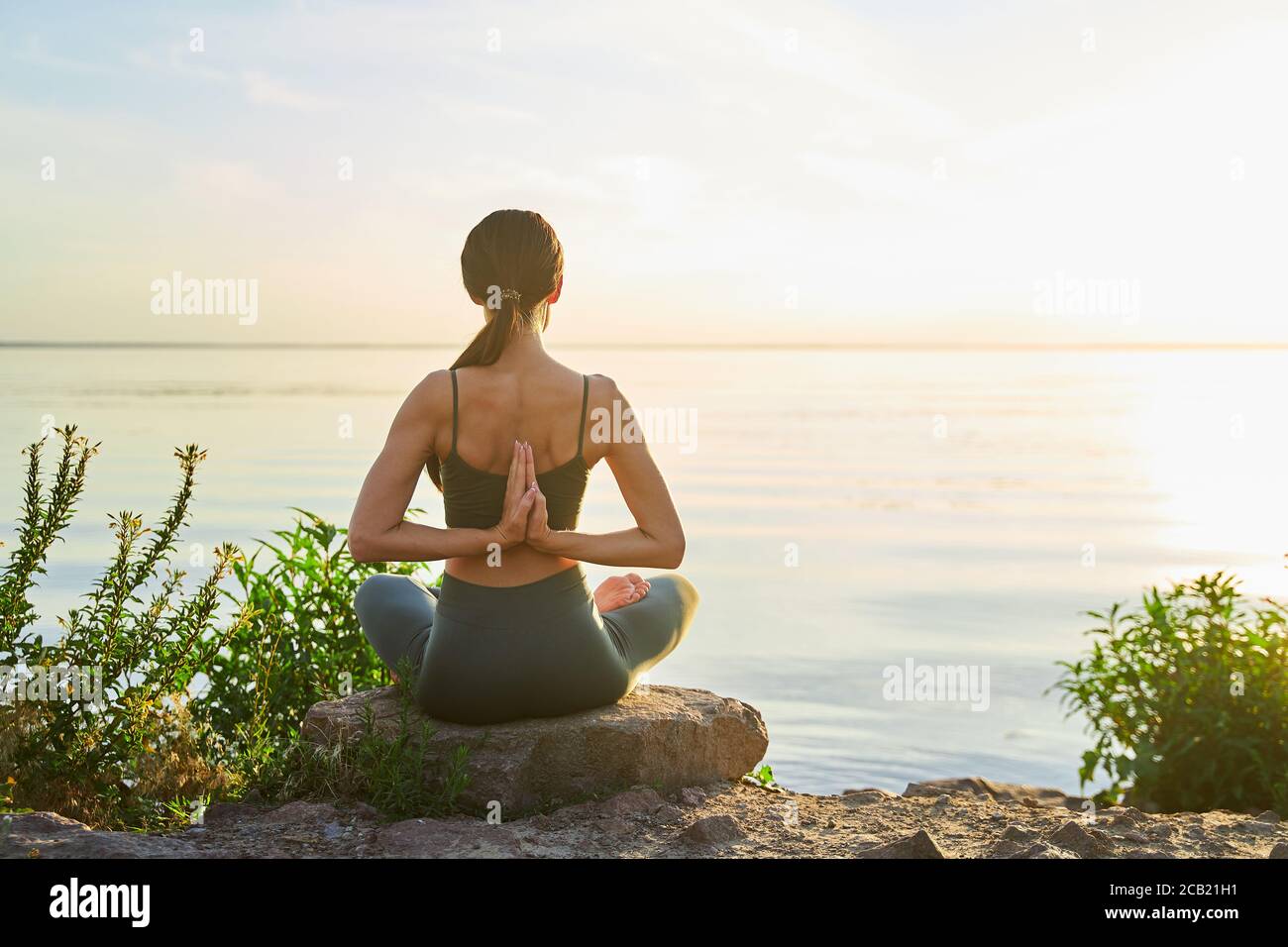 Sporty young woman doing reverse prayer pose outdoors by the sea Stock Photo