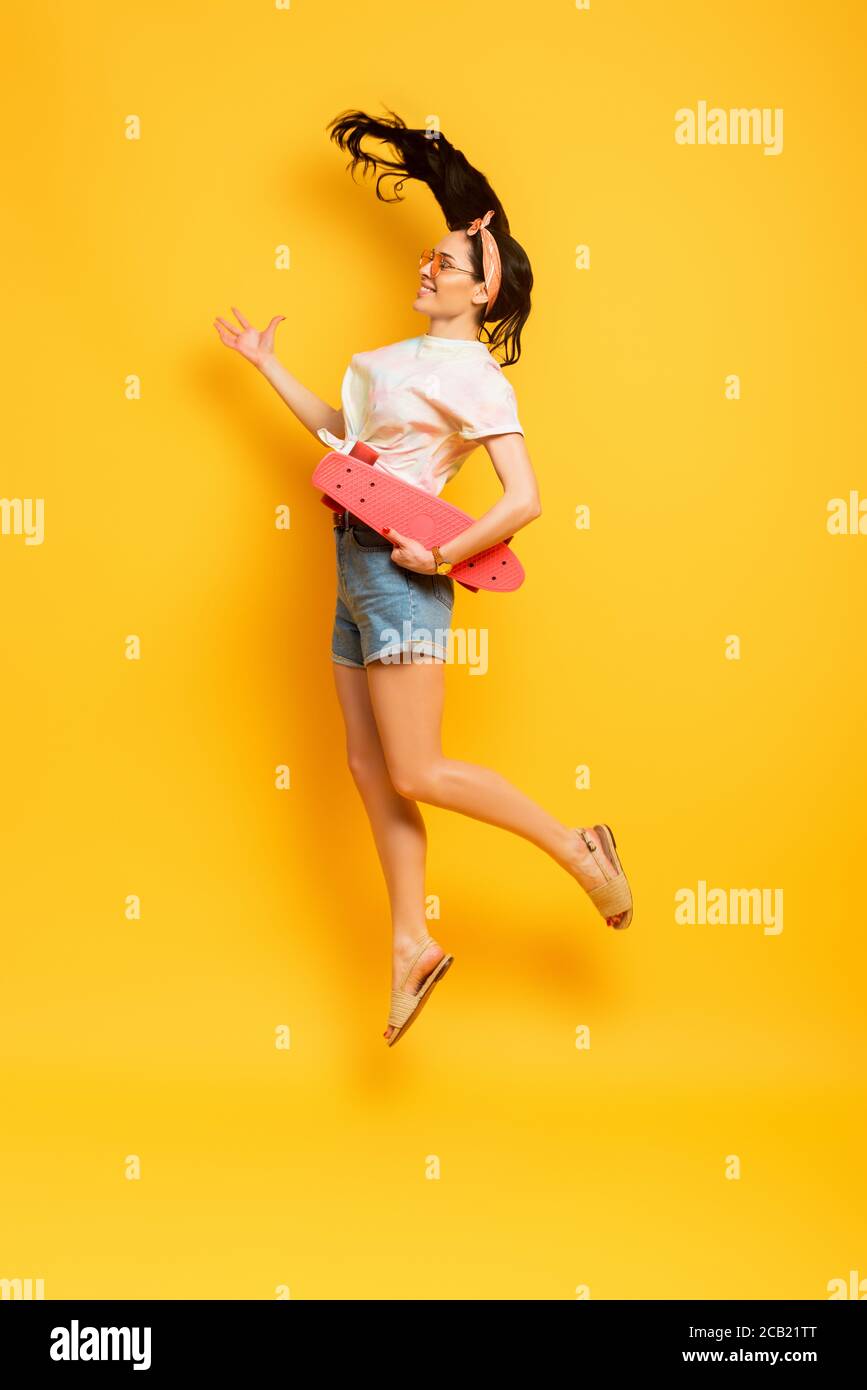 side view of happy stylish summer brunette girl jumping with pink penny ...