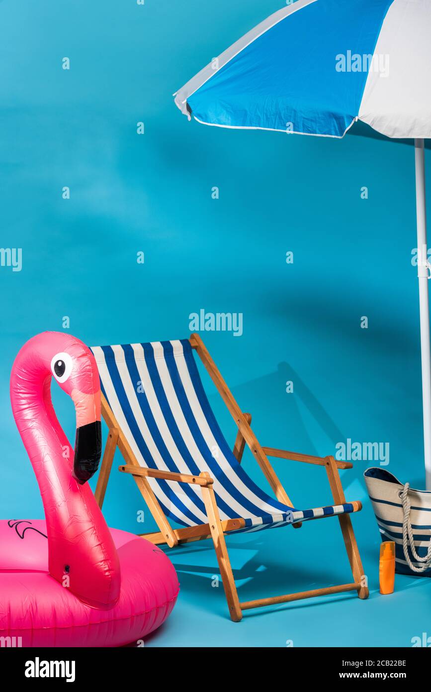 striped deck chair near inflatable flamingo sunscreen beach bag and umbrella on blue background Stock Photo Alamy