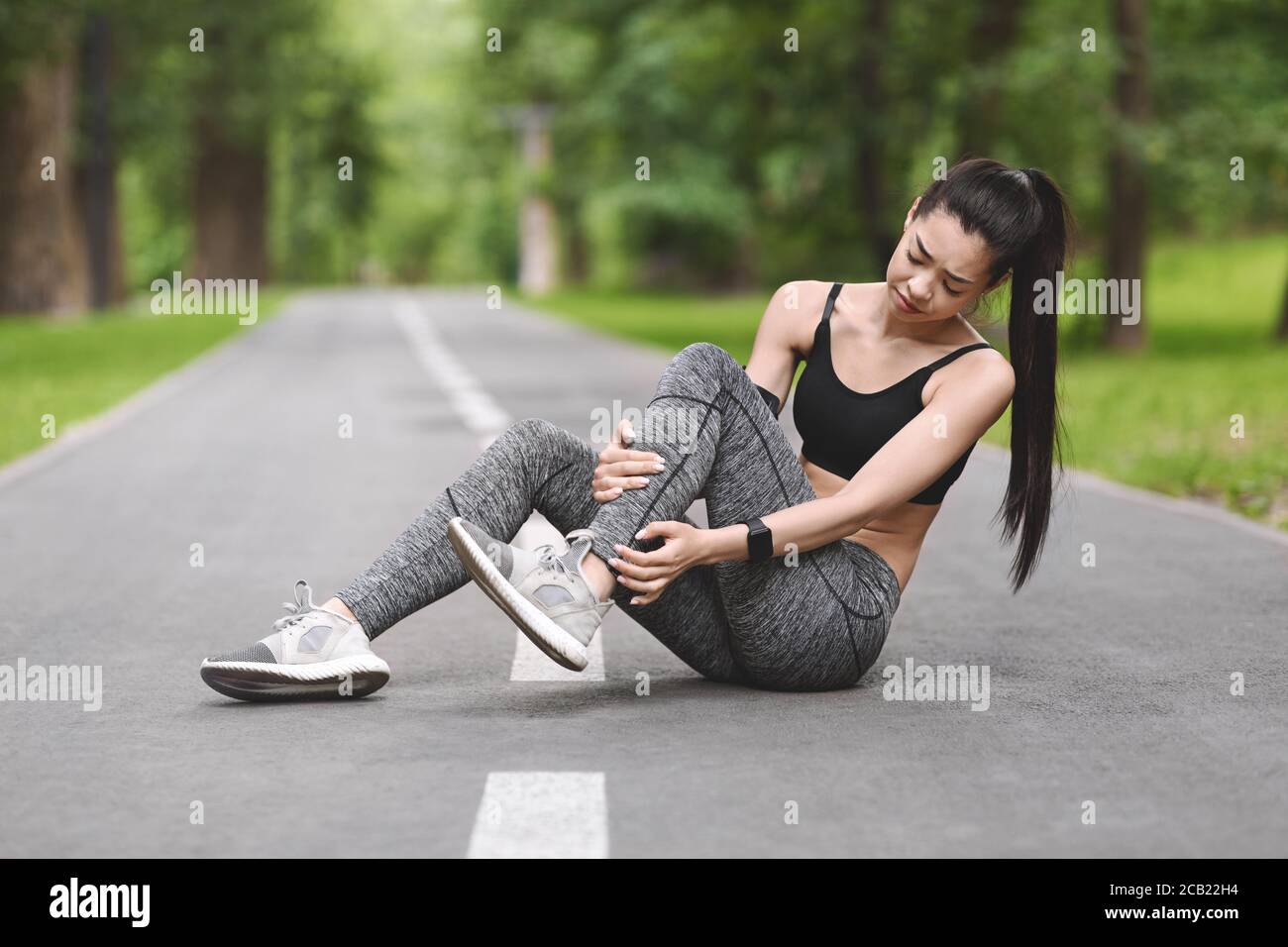 Sports Injury. Asian Girl Suffering From Ankle Pain After Jogging In Park Stock Photo