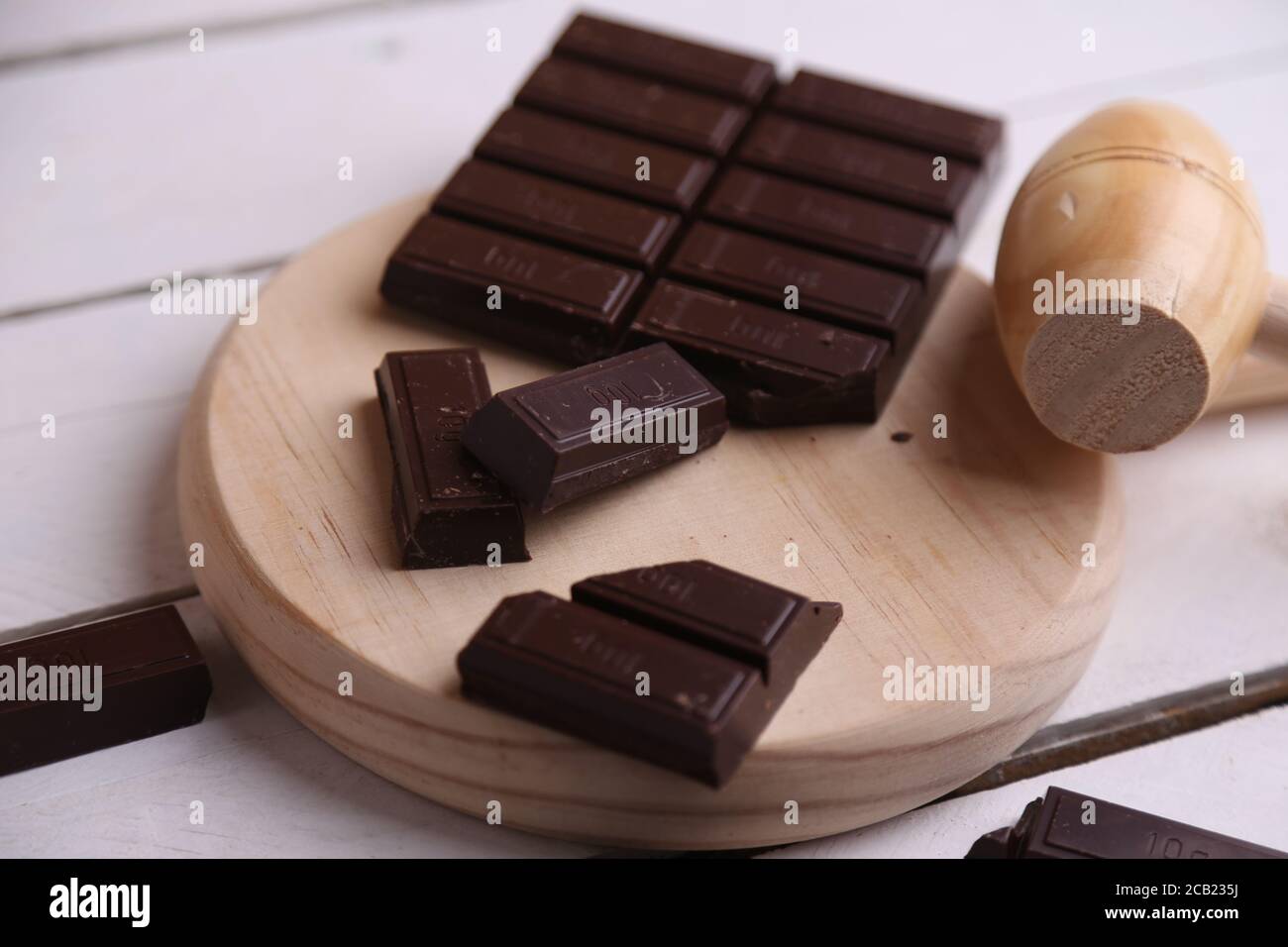 Closeup shot of a wooden small mallet near a bar of dark chocolate Stock Photo