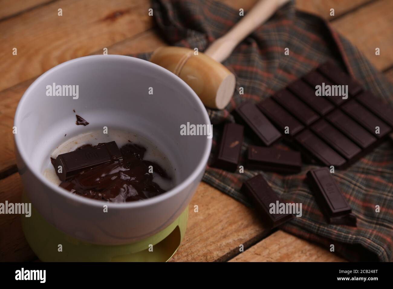 High angle shot of a wooden small mallet near a bar of dark chocolate and melted chocolate Stock Photo