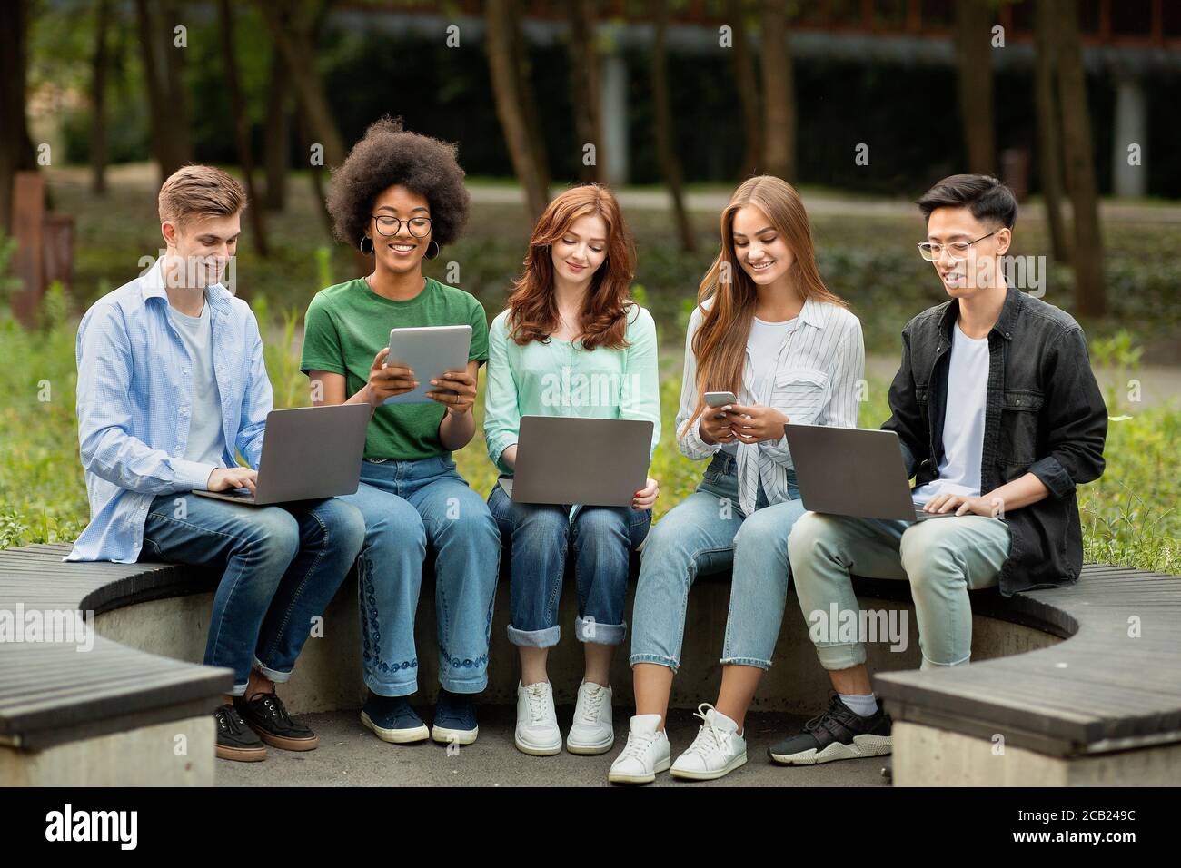 Modern Gadgets For Study. College Students Sitting Outdoors With Different Electronic Devices