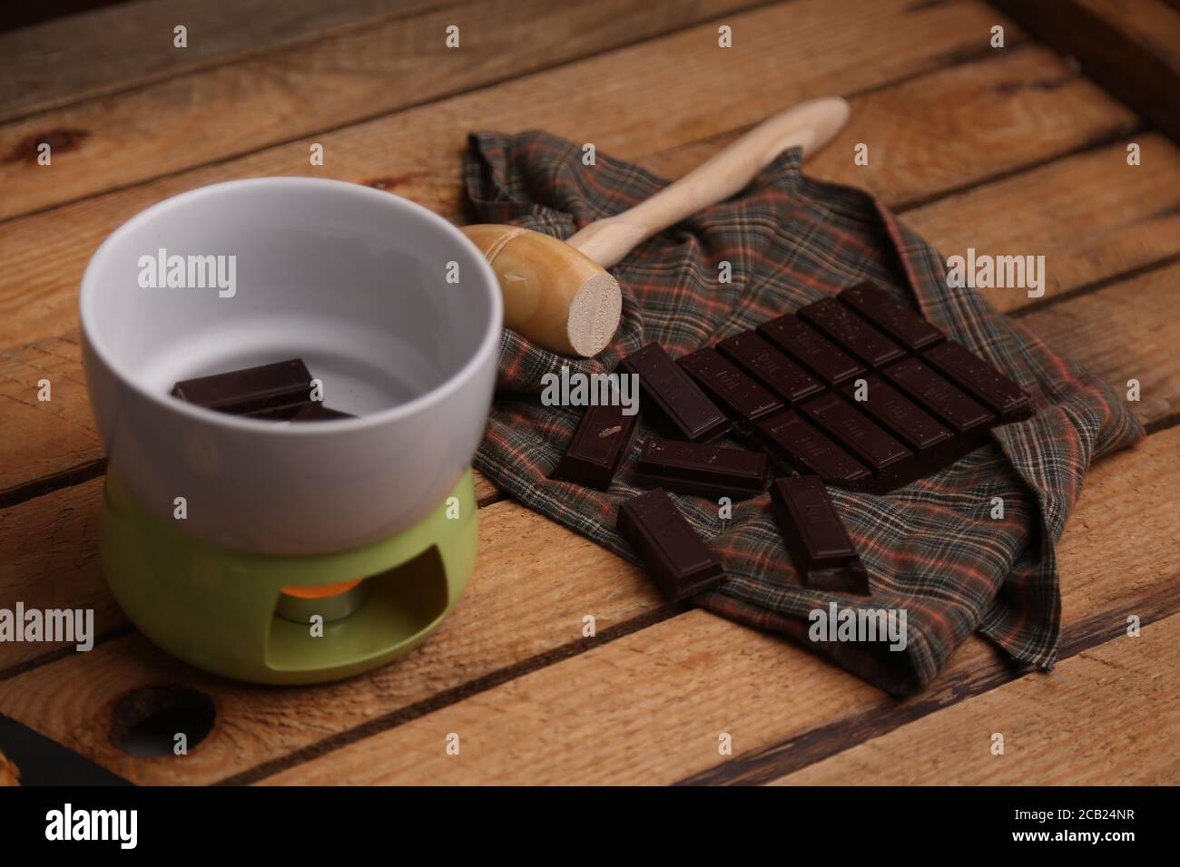 High angle shot of a wooden small mallet near a bar of dark chocolate and a bowl of chocolate Stock Photo