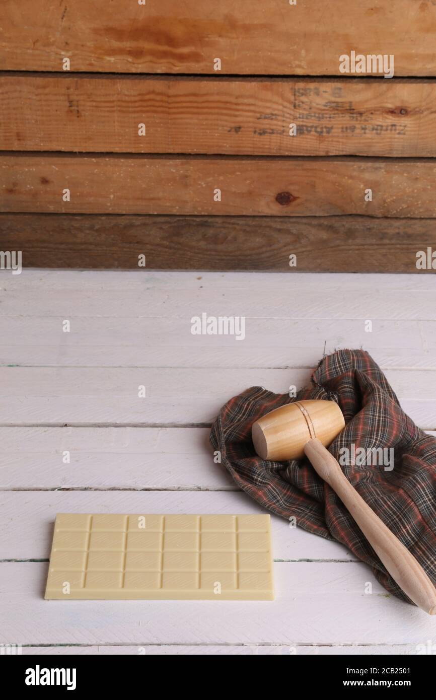 Vertical shot of a wooden small mallet near a bar of white chocolate Stock Photo