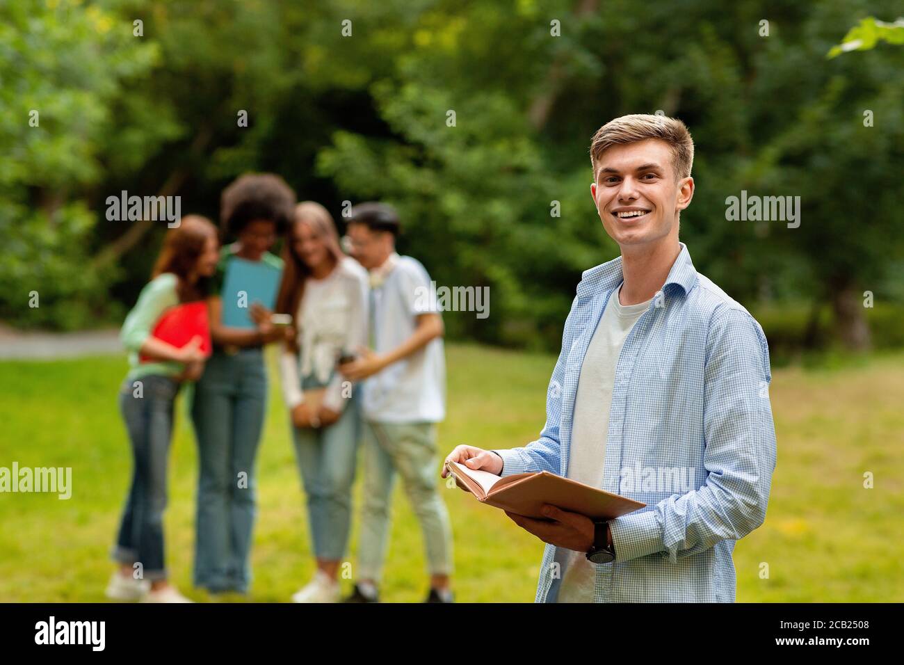 Student Guy Preparing For Exam Outdoor While His Friends Chatting On Background Stock Photo