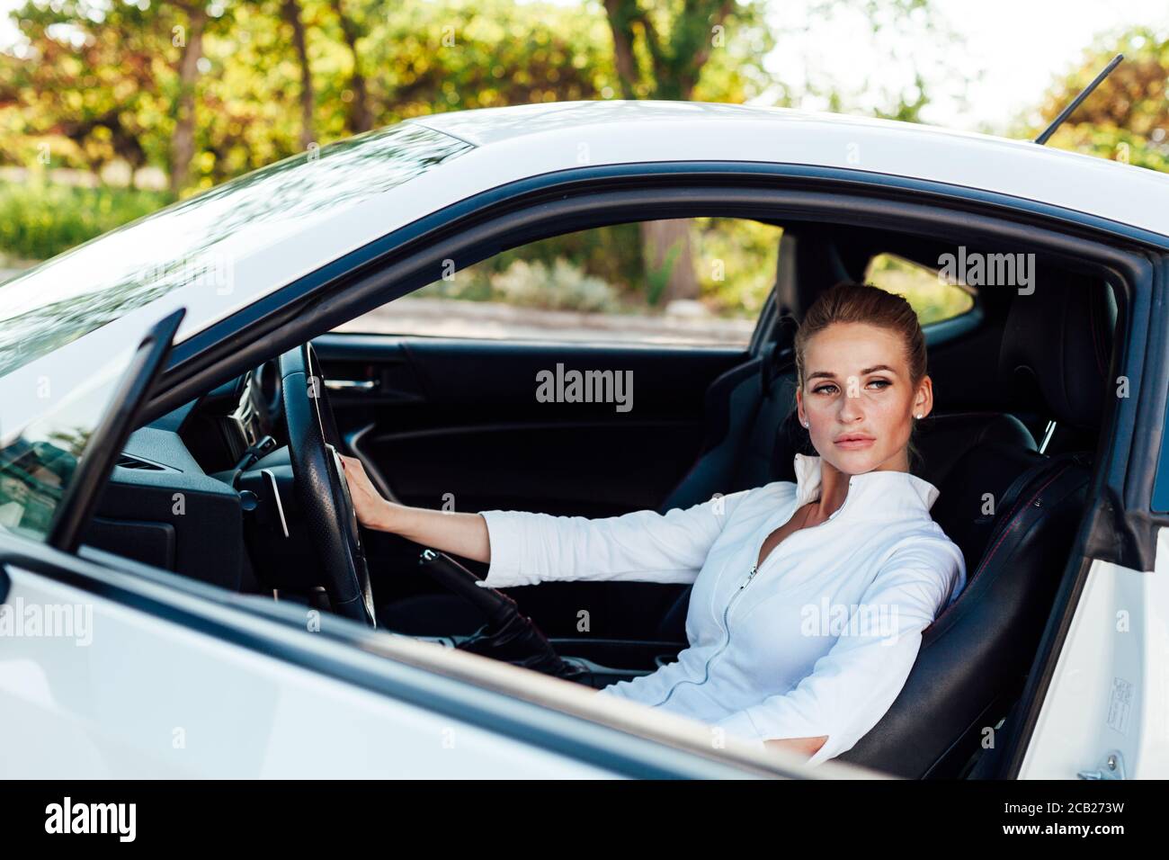 Beautiful female blonde driver behind the wheel of a white car Stock