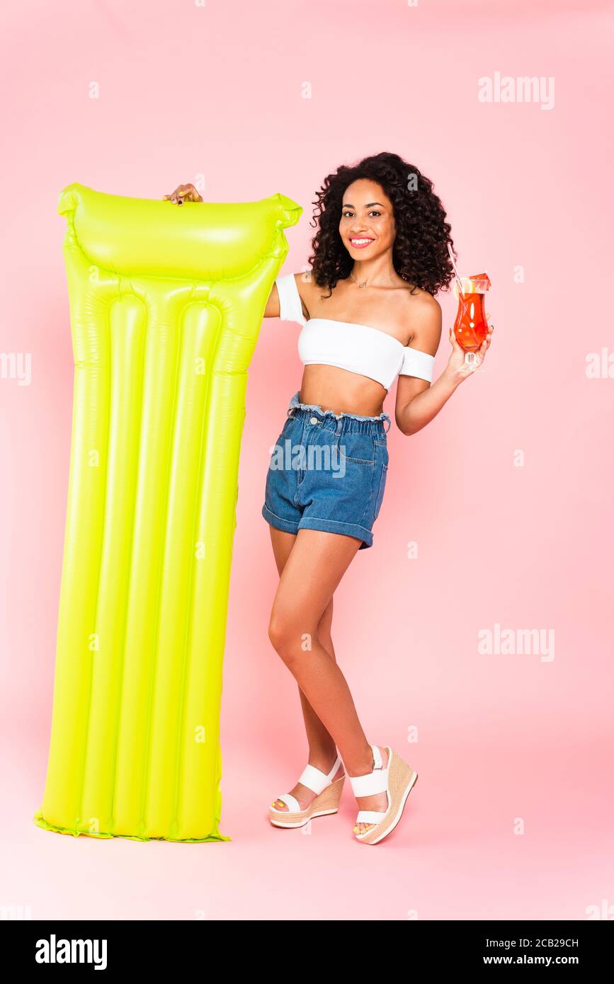 happy african american girl holding cocktail and inflatable mattress on pink Stock Photo