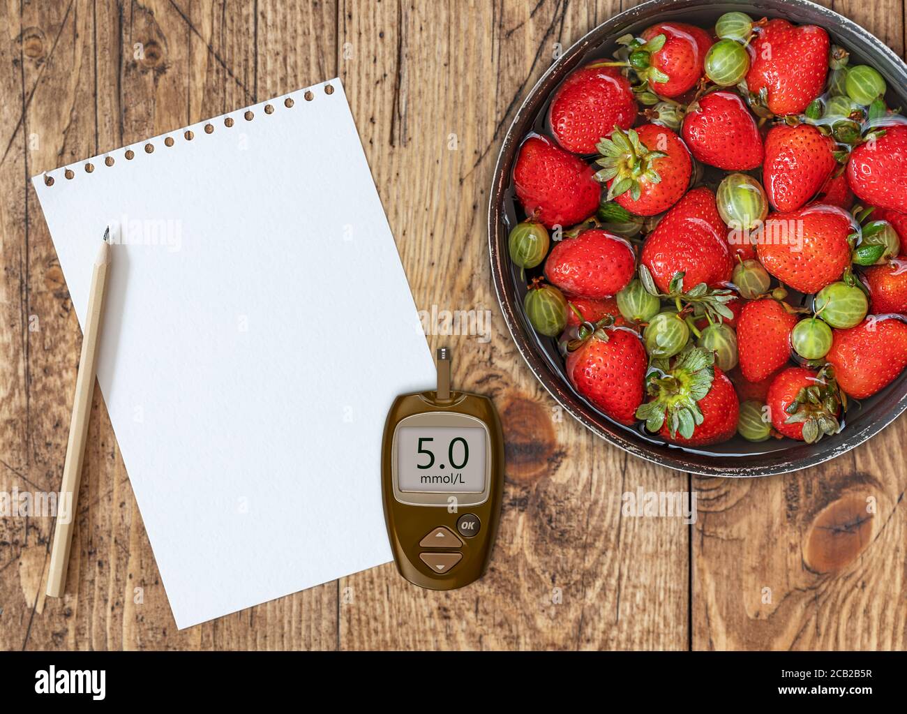 A bowl of ripe useful gooseberries, strawberries on wooden background with a glucose meter with a good glucose indicator Stock Photo