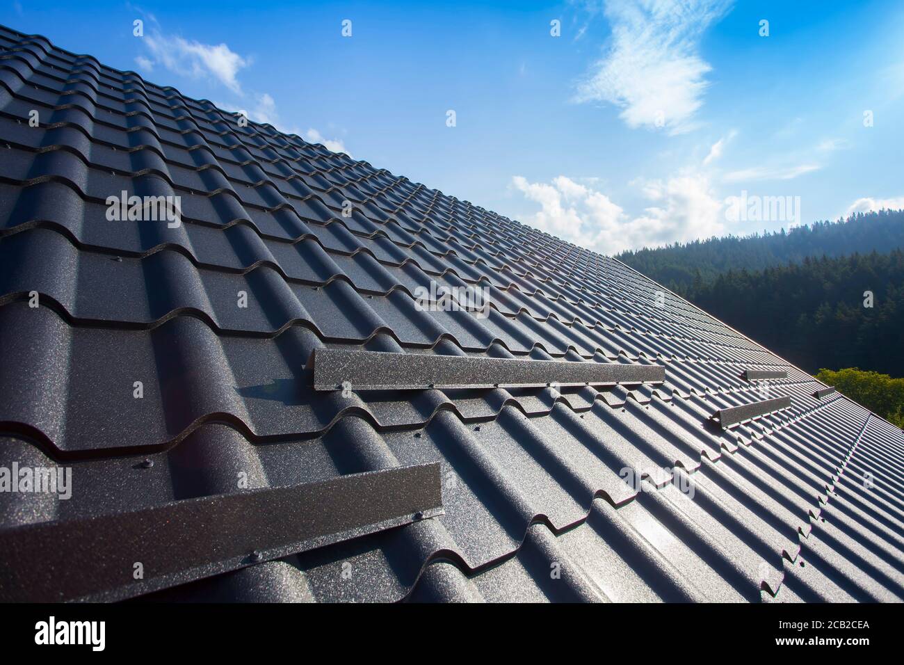 Roof repair, worker with white gloves replacing gray tiles or shingles on  house with blue sky