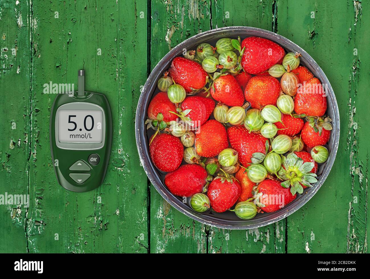 Fresh natural strawberries and gooseberries in a bowl with a glucose meter with a good glucose indicator Stock Photo