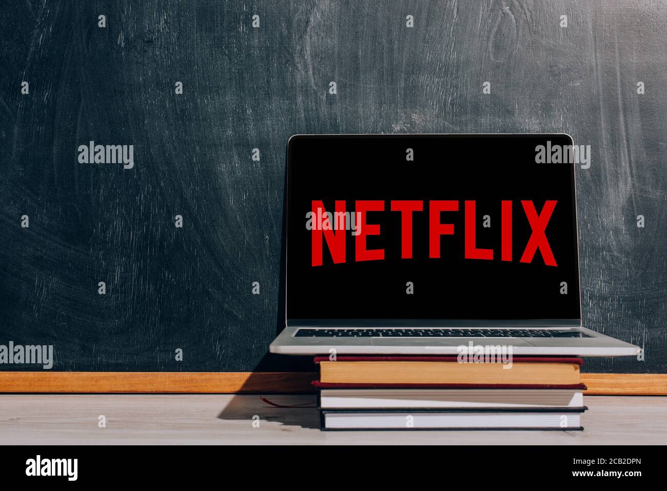 KYIV, UKRAINE - JULY 7, 2020: Laptop with Netflix website on stack of books near black chalkboard Stock Photo