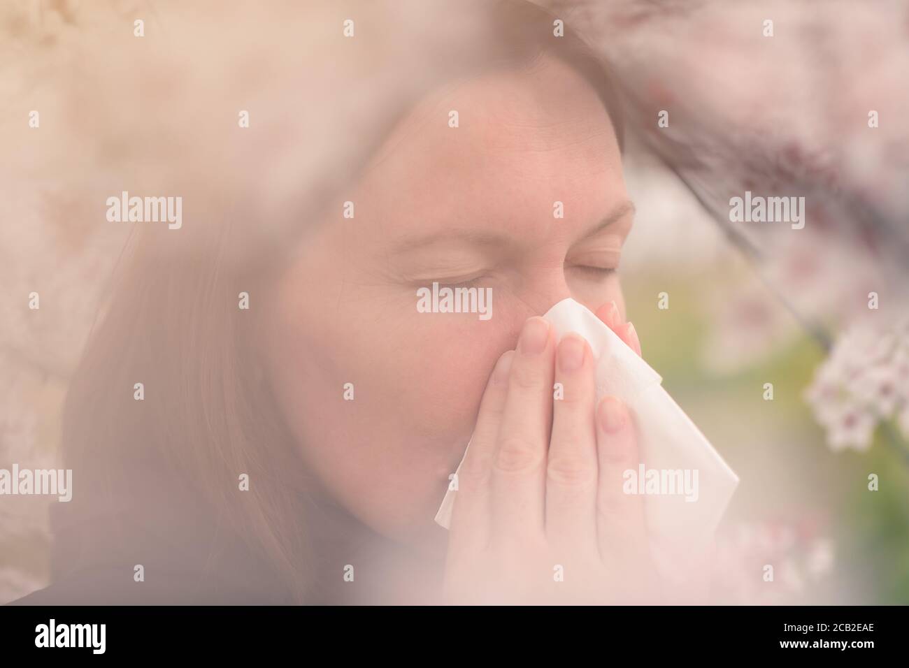 Tree pollen allergy in springtime concept, woman blowing and wiping her nose with paper handkerchief Stock Photo