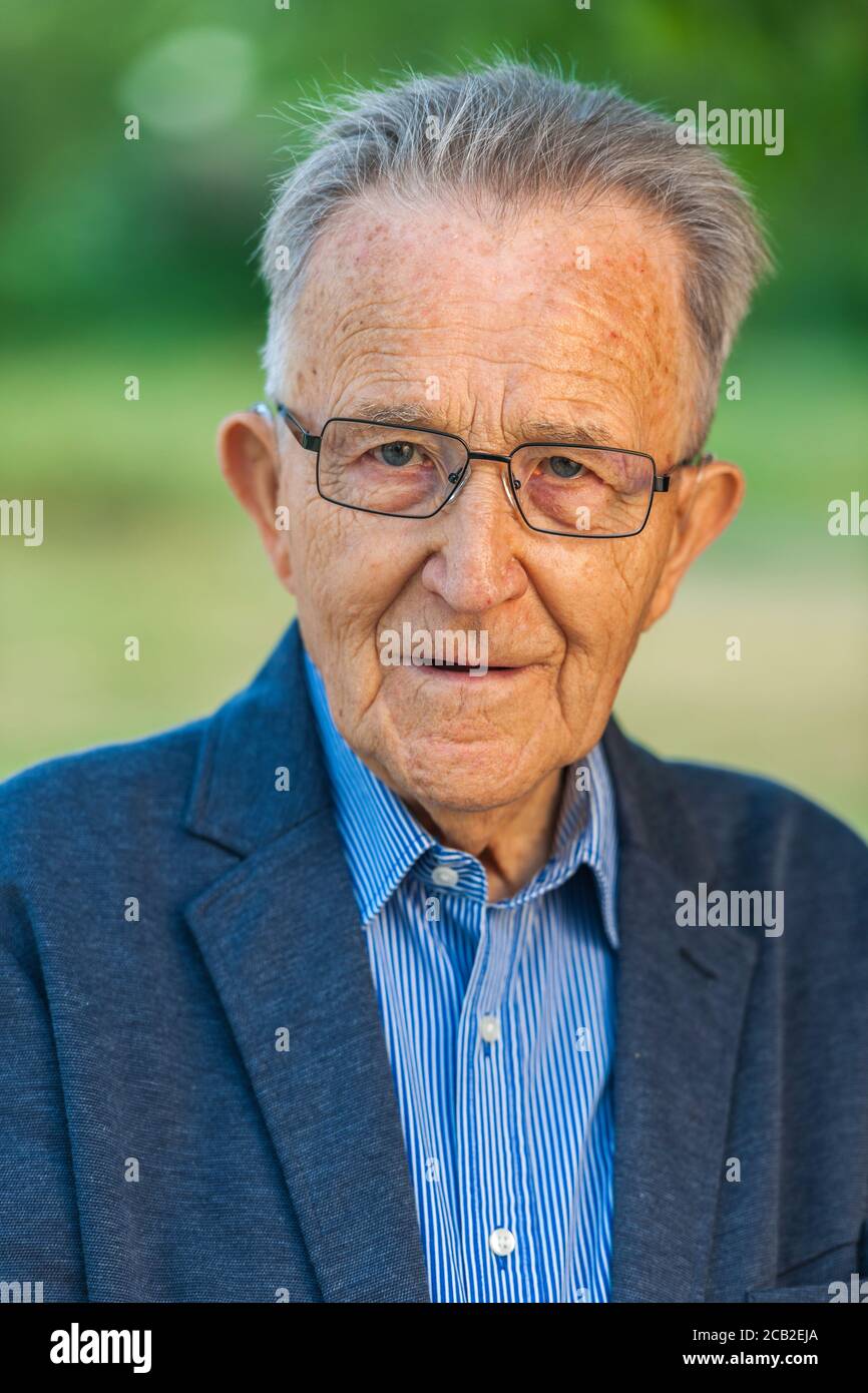 Headandshoulder portrait of an 80yearold man with glasses in a blue jacket in front of a