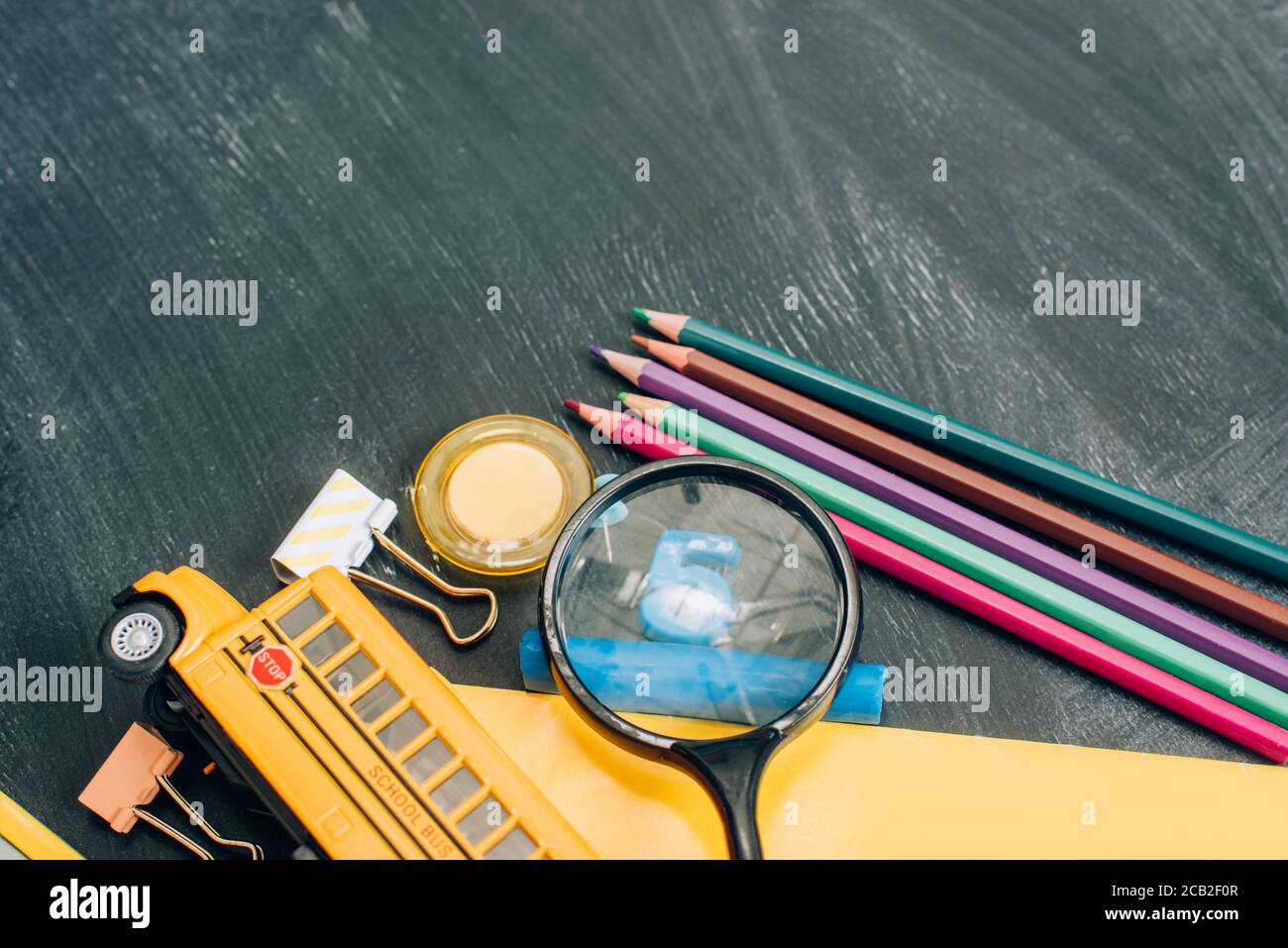 top view of school bus model, magnifier and school supplies on black ...