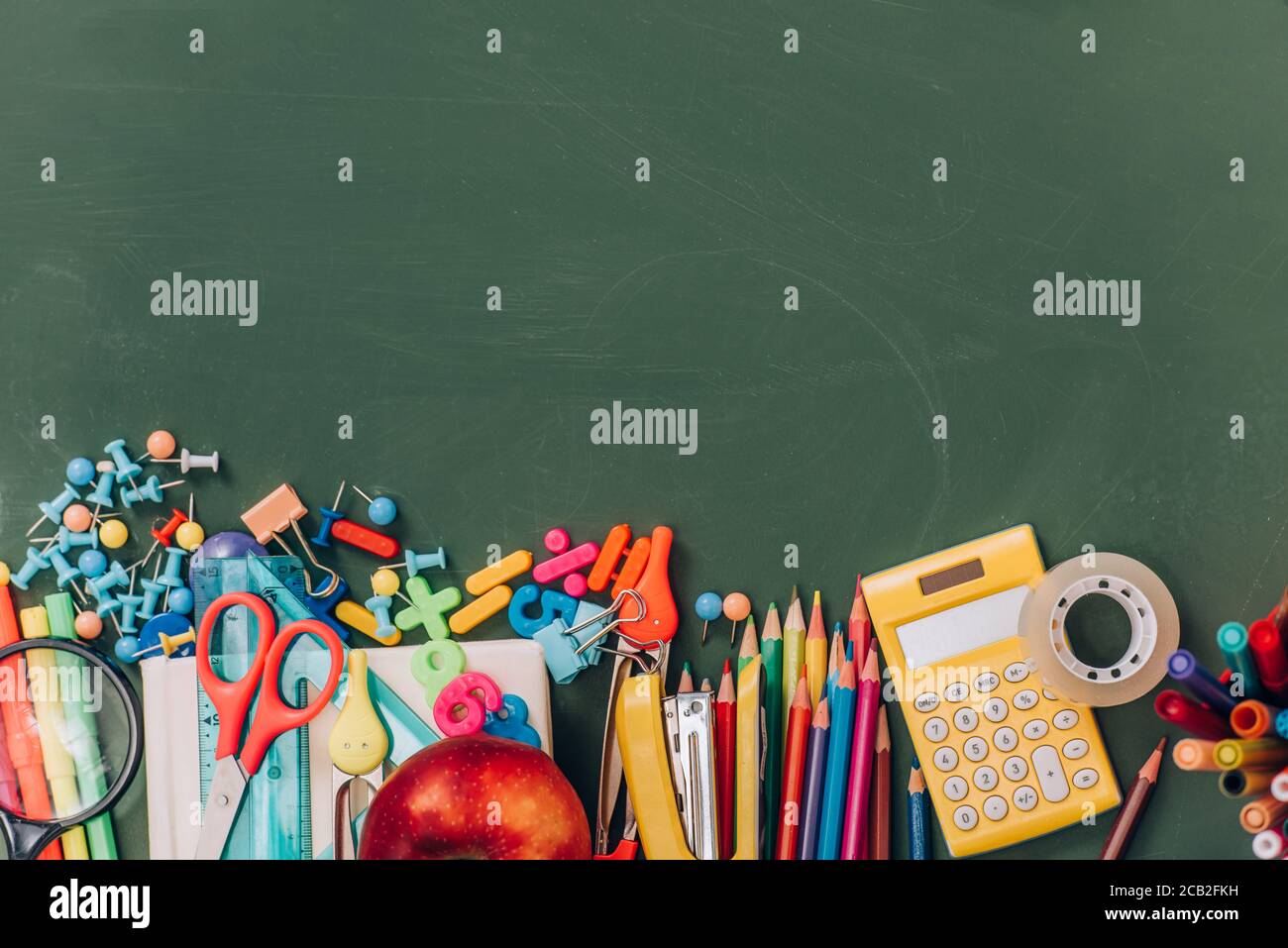 top view of apple, calculator and school supplies on green chalkboard ...
