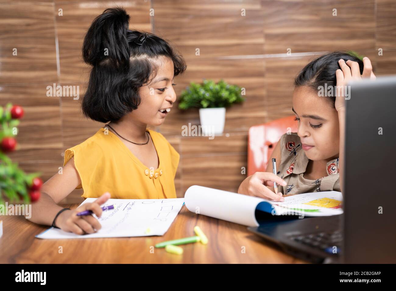 Two kid siblings busy in talking during e-learning or online class - concept of homeschooling or remote classroom at home during covid-19 or Stock Photo