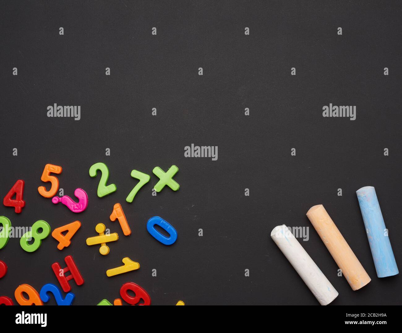 multicolored chalks on lie on empty black chalk board, top view, back to school Stock Photo