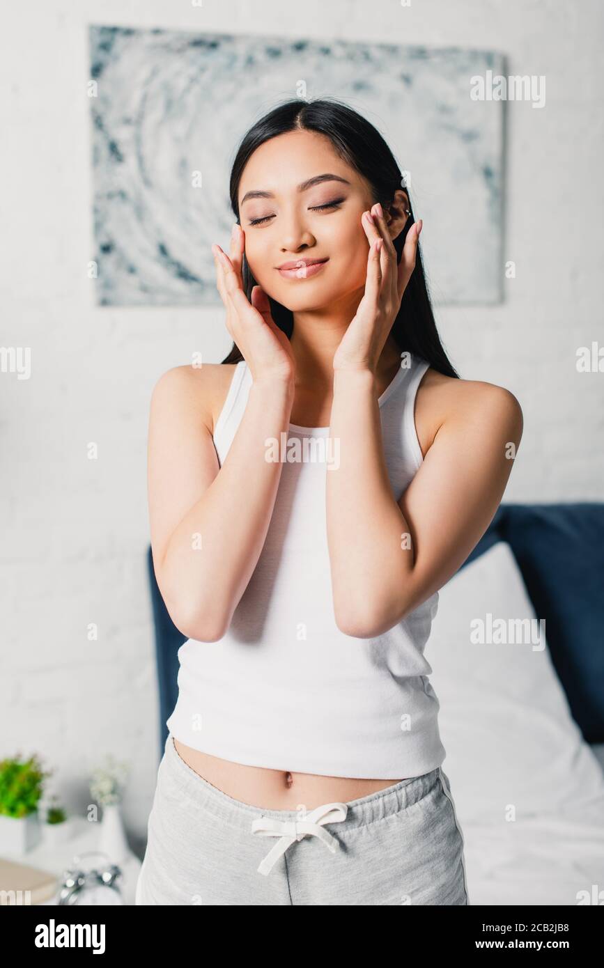 Young asian woman with closed eyes touching face in bedroom Stock Photo ...