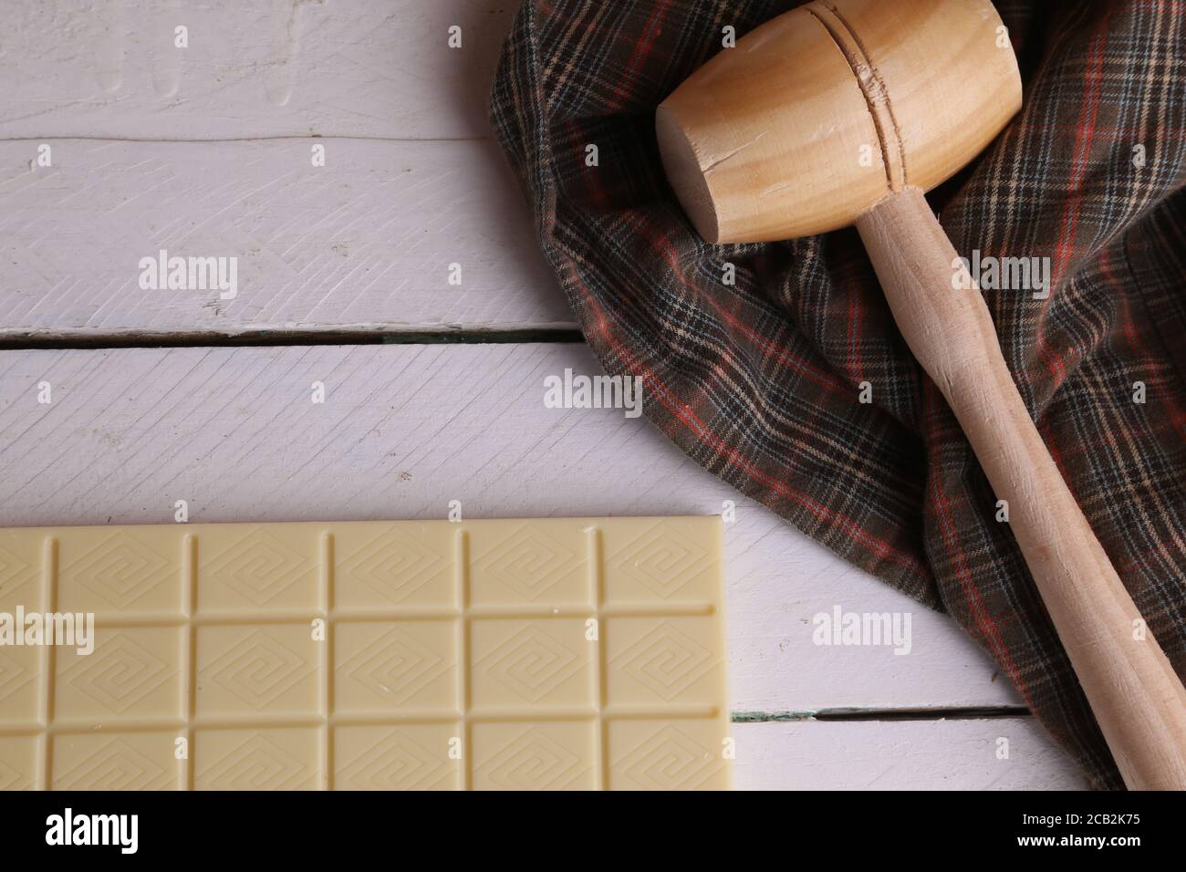 Overhead shot of a wooden small mallet near a bar of white chocolate Stock Photo