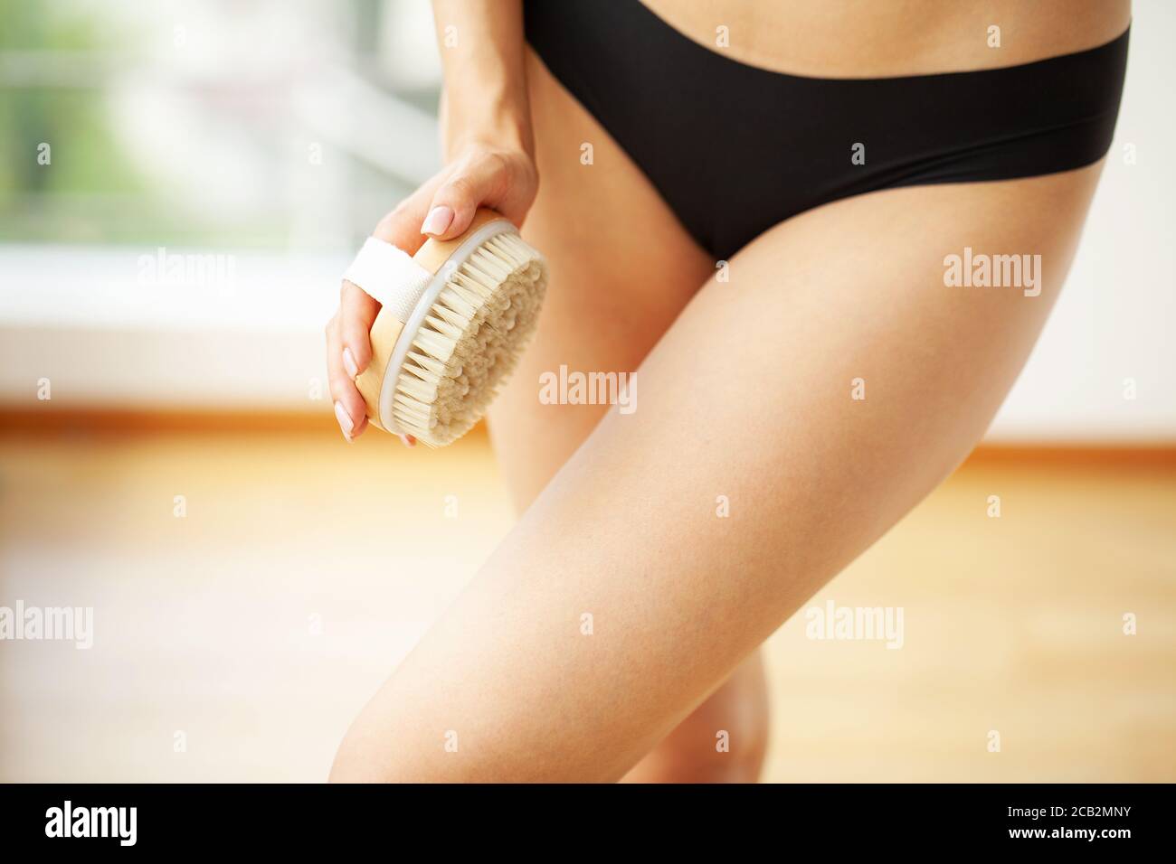 Woman arm holding dry brush to top of her leg, cellulite treatment and