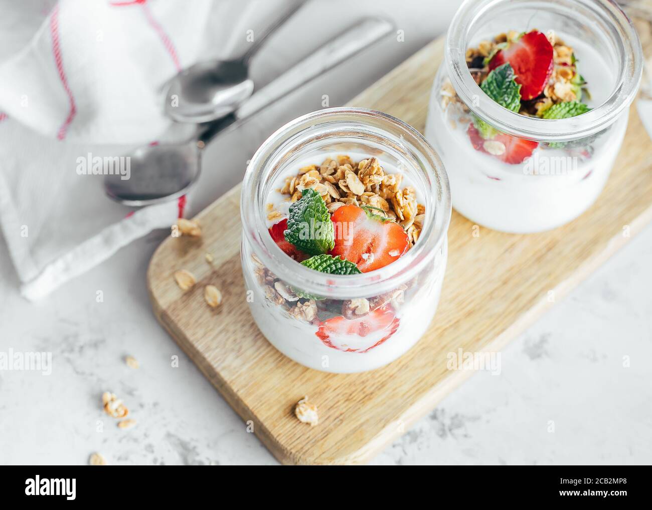 Two jars with tasty parfaits made of granola, strawberries and yogurt on white marble table. Stock Photo