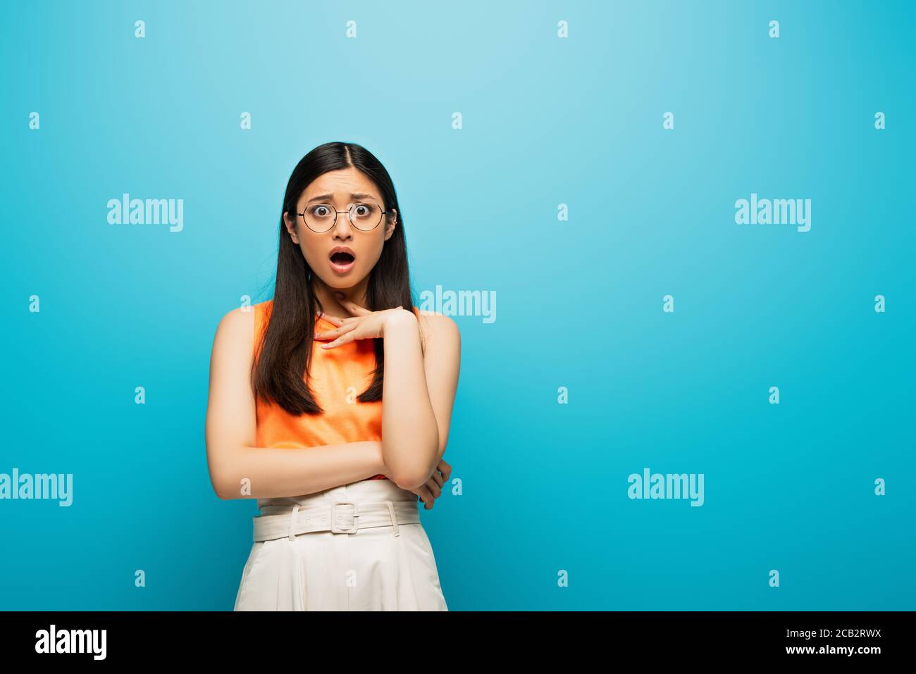 surprised asian woman in glasses standing on blue Stock Photo