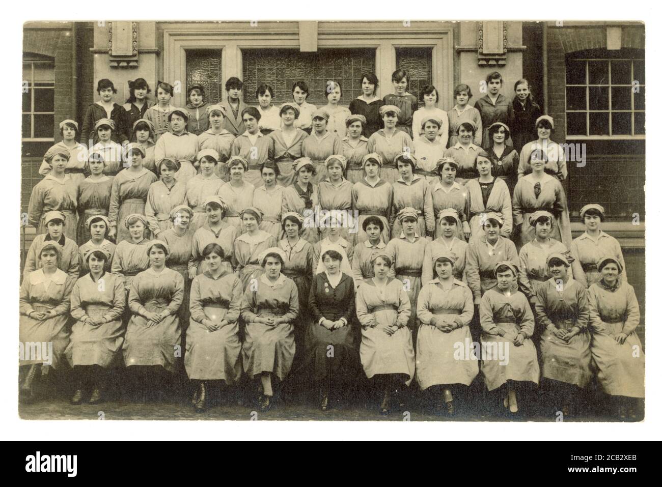 Original WW1 era postcard of female hospital  war workers, young women, wearing uniforms and mob caps, a matron sits in the front row, possibly hospital orderlies U.K. circa 1916 Stock Photo