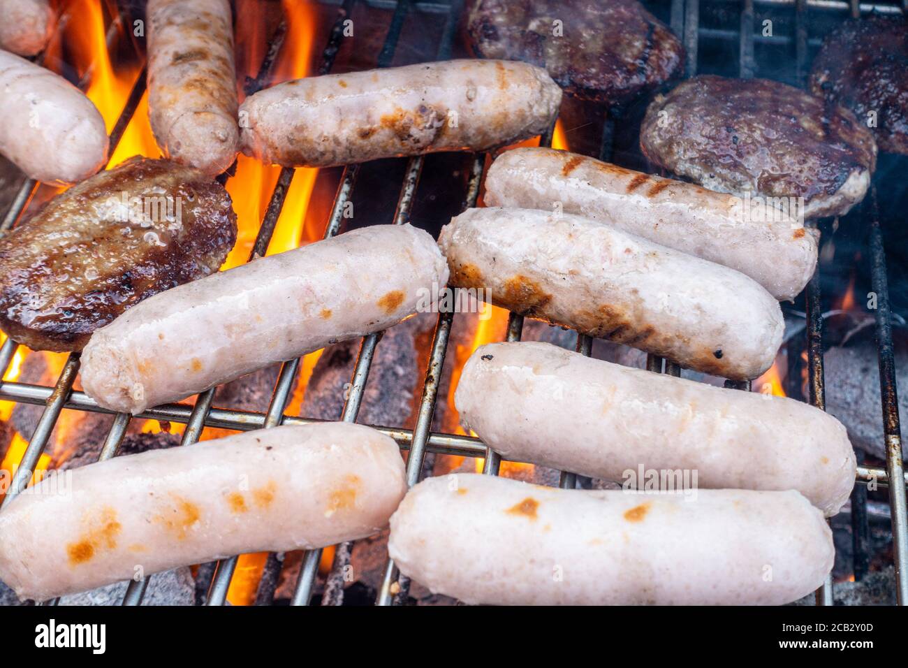 Sausage and beef burgers cooking on a barbecue. Stock Photo