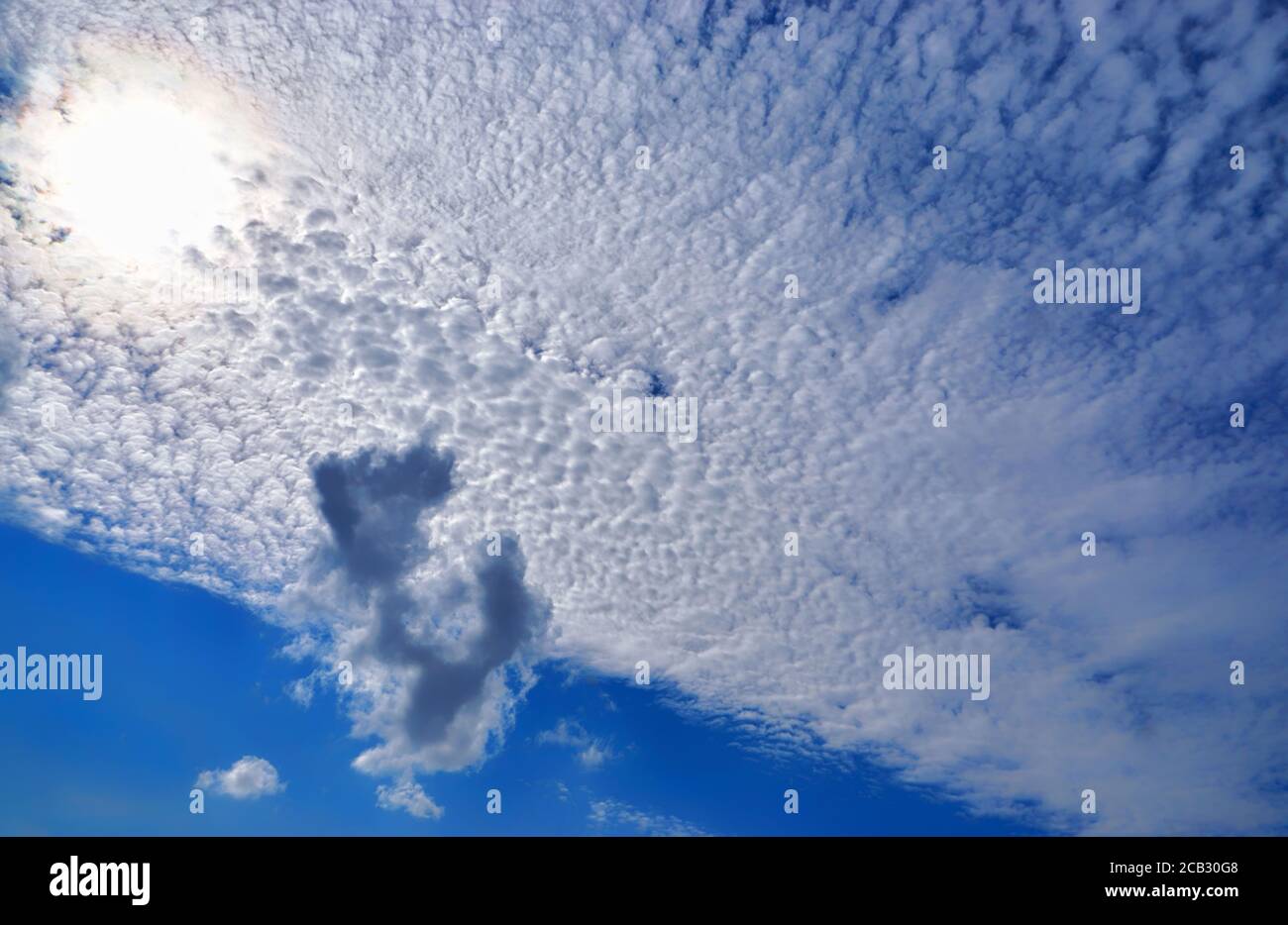 The blue sky is covered with white clouds and the sun shines through ...