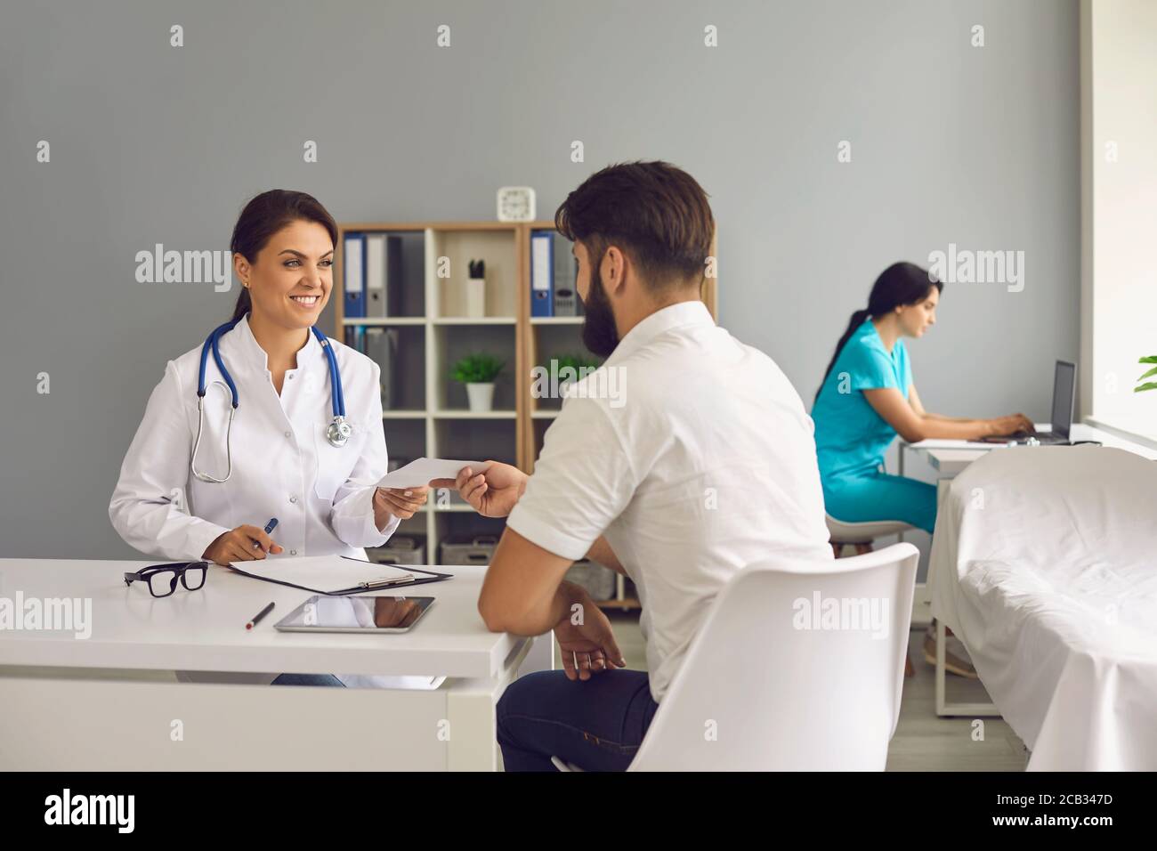 The doctor gives the patient a prescription while sitting at the table ...