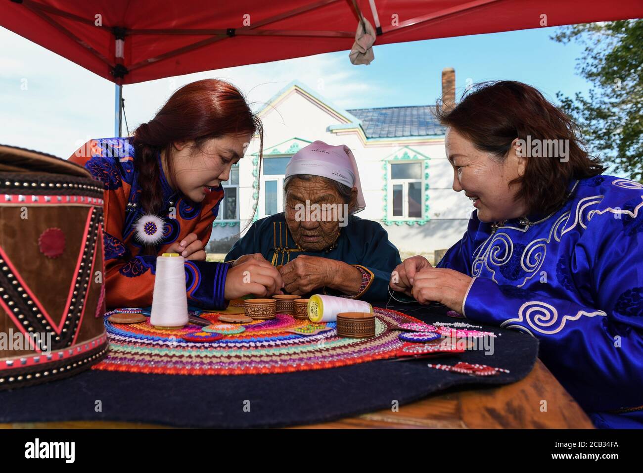 (200810) -- HULUN BUIR, Aug. 10, 2020 (Xinhua) -- Aijim (L) learns the method of making 'Sun Flower' from her grandmother (C) in Ewenki Autonomous Banner, north China's Inner Mongolia Autonomous Region, Aug. 6, 2020.  Aijim is a post-90s girl of Ewenki ethnic group living in Inner Mongolia Autonomous Region. In 2014, she returned to her hometown at Ewenki Autonomous Banner, Hulun Buir City, after graduation from university, and helped her mother Uran run a handicraft studio. They make handicrafts themed on 'Sun Flower', and opened up online business to sell the products.     'Behind the handic Stock Photo