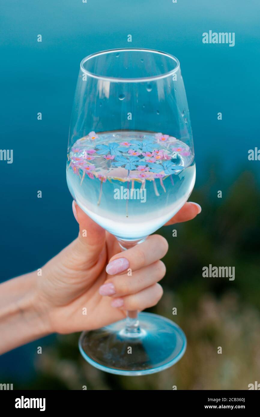 A beautiful hand with a ring holds a glass against the background of the sea. Stock Photo