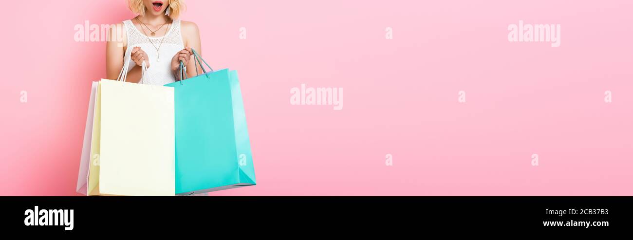 horizontal crop of surprised woman in white dress holding shopping bags ...