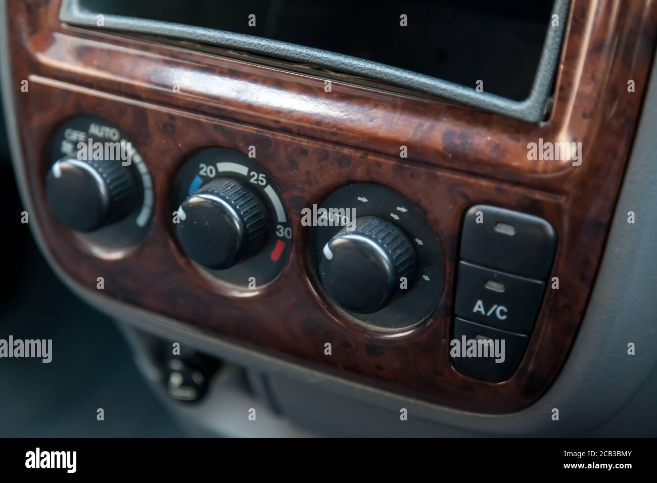 The central control console on a brown decorated panel inside the car close-up with buttons and climate control toggle switches. Stock Photo