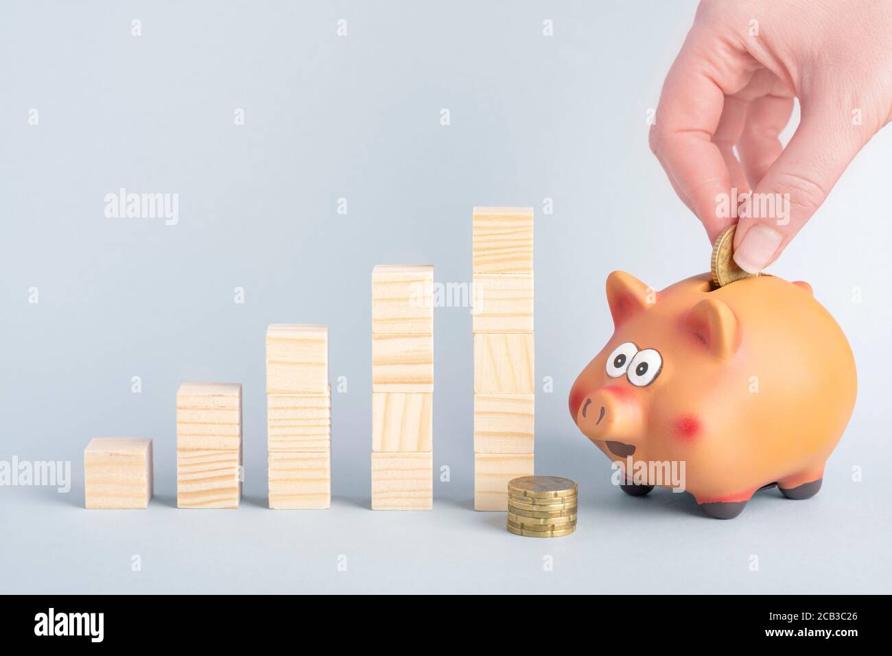 A hand puttiing a coin into a piggy bank and growth graph concept from wooden blocks Stock Photo