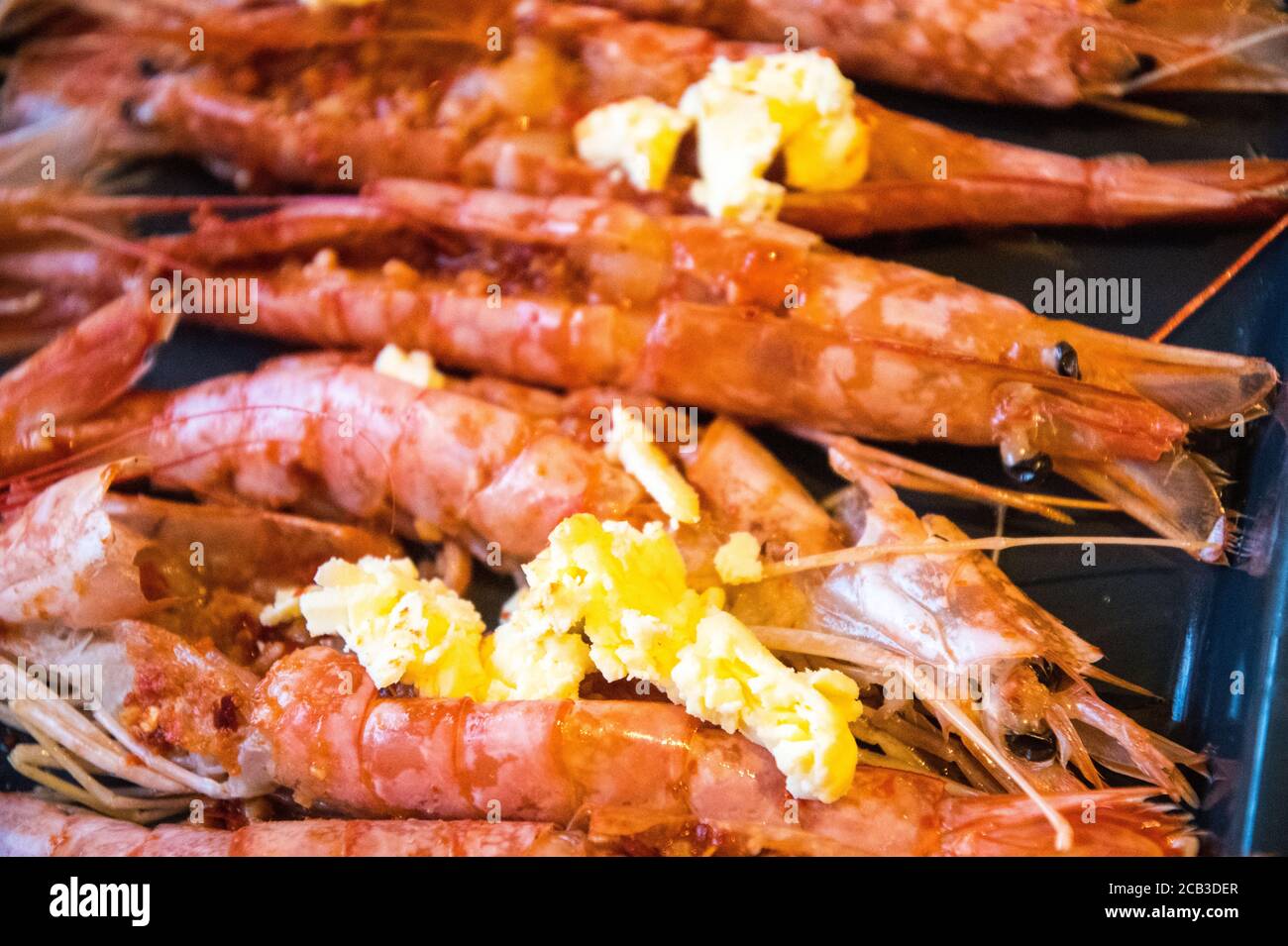 A platter of large, king-sized prawns in black and white and monochrome. They prepared in garlic butter for grilling and devouring. De-veined prawns, a blob of garlic butter, and freshly prepared. Stock Photo