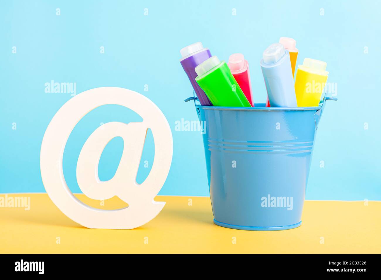 A metal bucket with highlighter marker pen and at symbol or commercial at on a blue background. Back to school Stock Photo