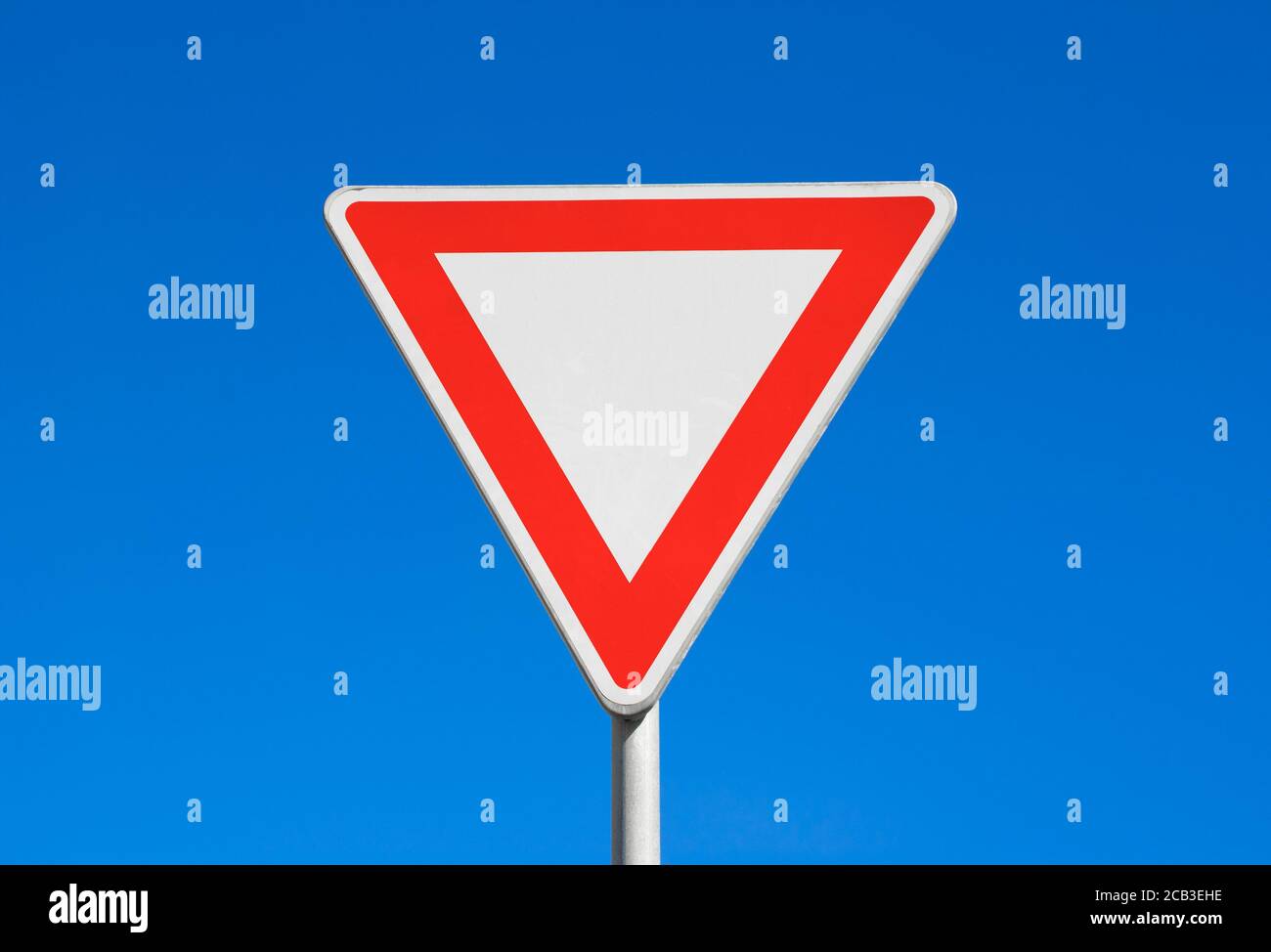 Give way / Yield - red and white triangle. Clear blue sky is behind road sign. Stock Photo