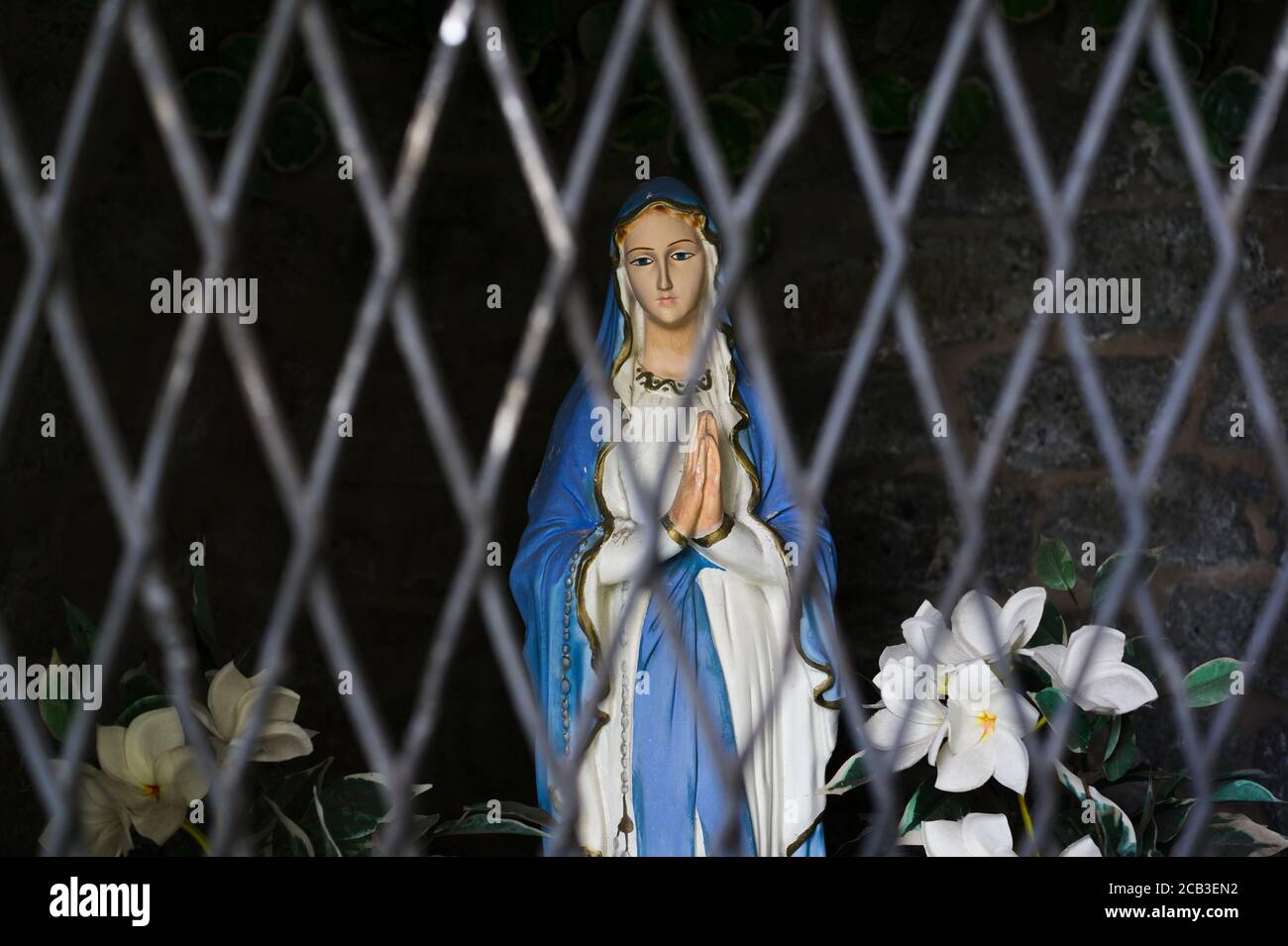 Statuette of Virgin Mary is hidden behind the bars. Metaphor Negative