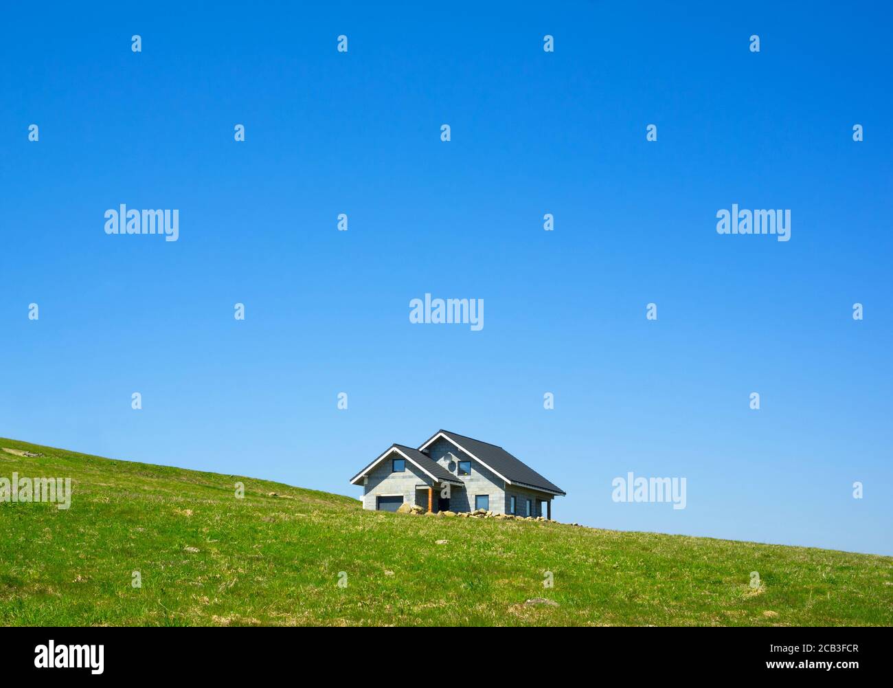 Construction and building of new residential house. Property is unfinished yet - unplastered walls with visible bricks. Hillside and empty meadow and Stock Photo
