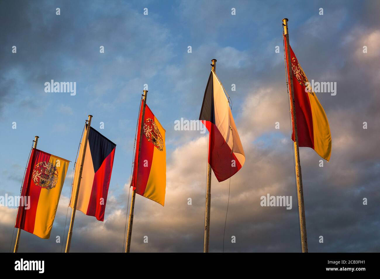 National flag of Czech Republic and Flag with coat of arms of City of Prague. Sky with dark stormy clouds in the background. Yellow evening light Stock Photo